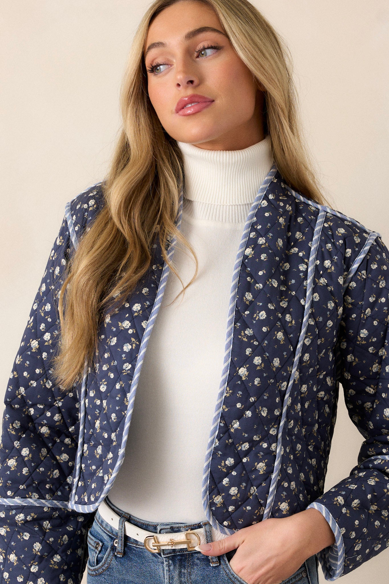 This navy jacket features an open front, a rounded neckline, a small floral pattern, a blue and white striped interior, a quilted material, a blue and white striped trim and long sleeves.