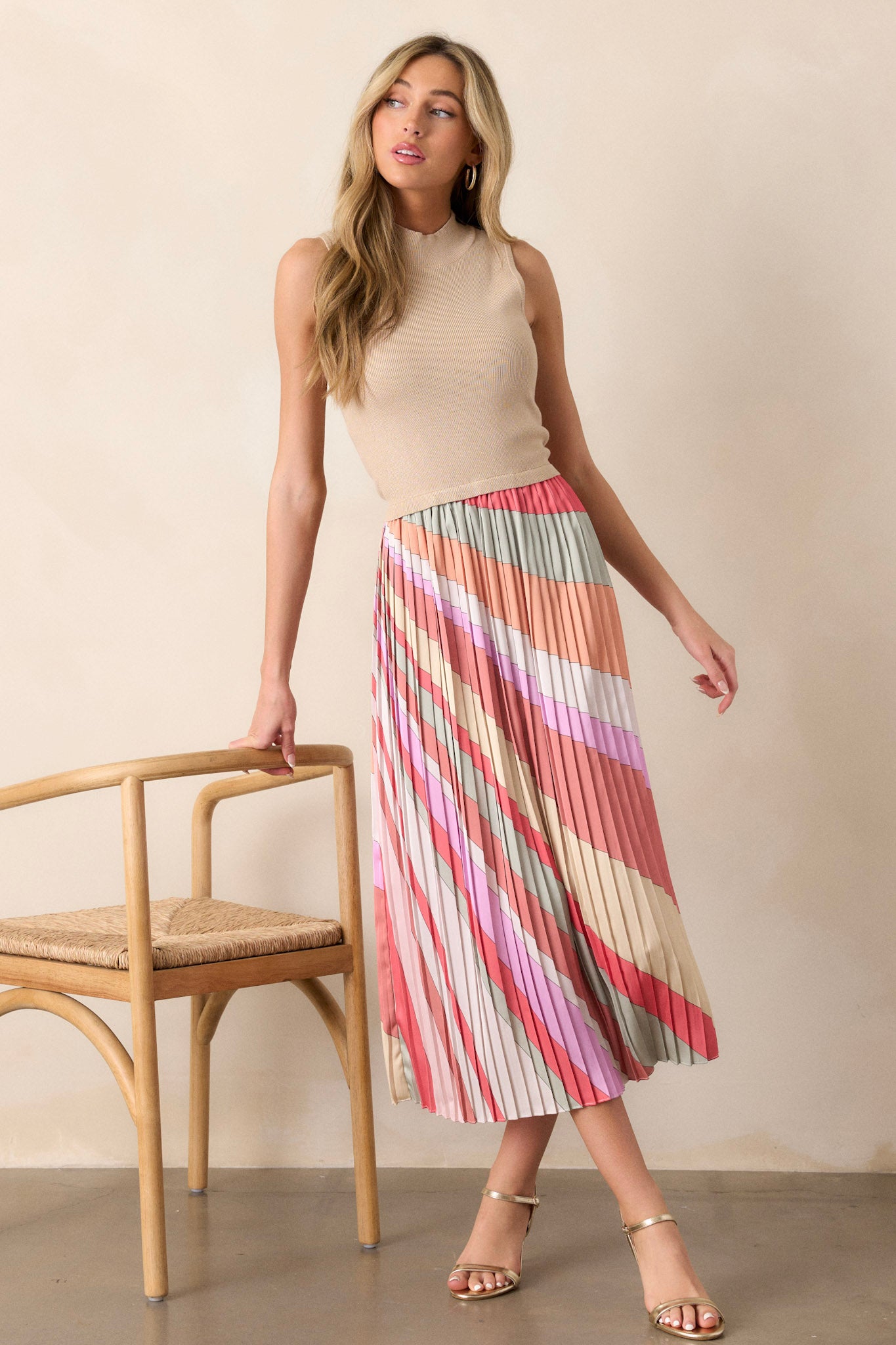 This taupe midi dress features a high neckline, a ribbed sweater like bodice, a multi color pleated skirt, a sleeveless design, and a flowing silhouette.