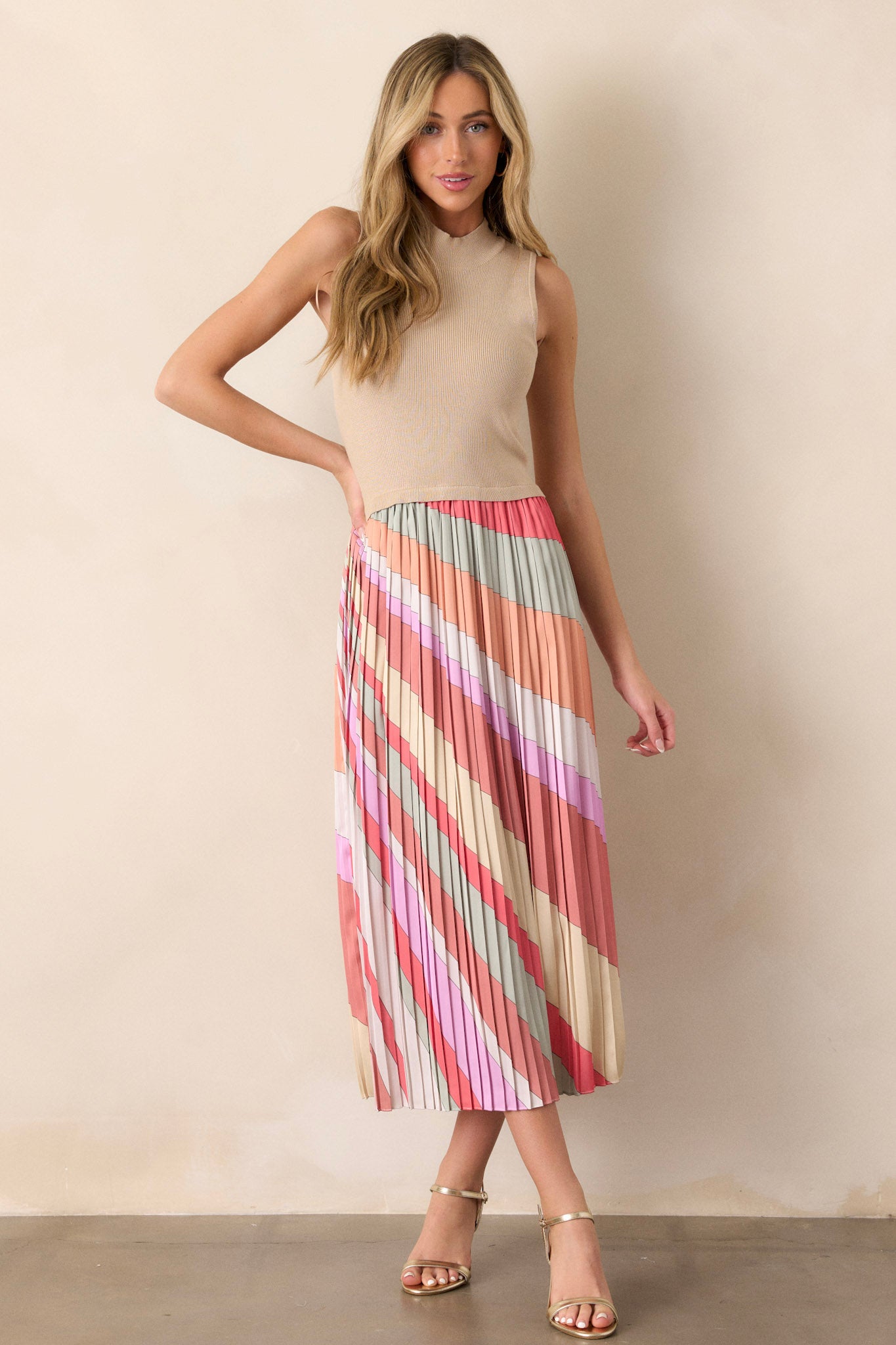 Full length view of a taupe midi dress with a high neckline, a ribbed sweater-like bodice, a multi-color pleated skirt, a sleeveless design, and a flowing silhouette