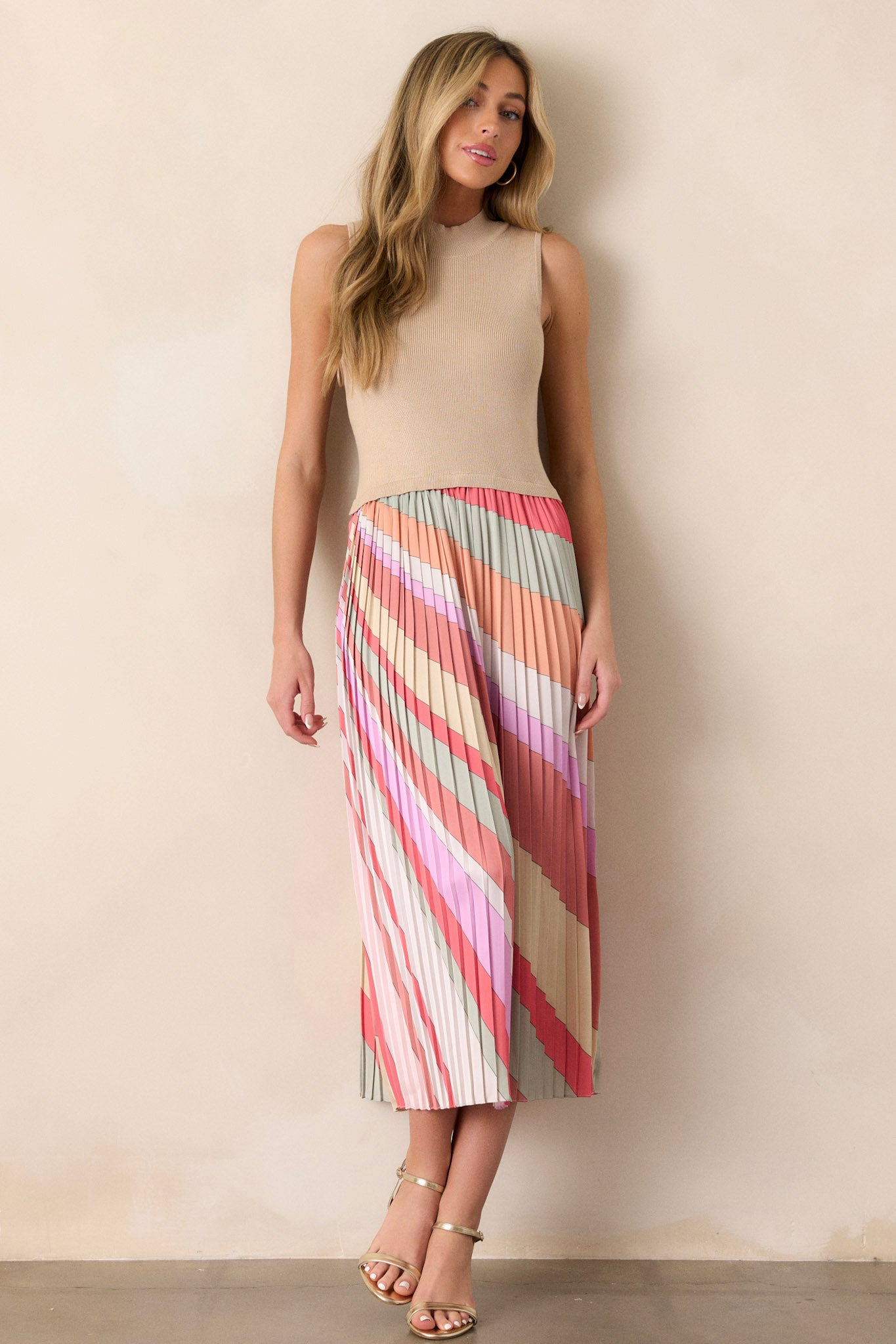 Front view of a taupe midi dress featuring a high neckline, a ribbed sweater-like bodice, a multi-color pleated skirt, a sleeveless design, and a flowing silhouette.