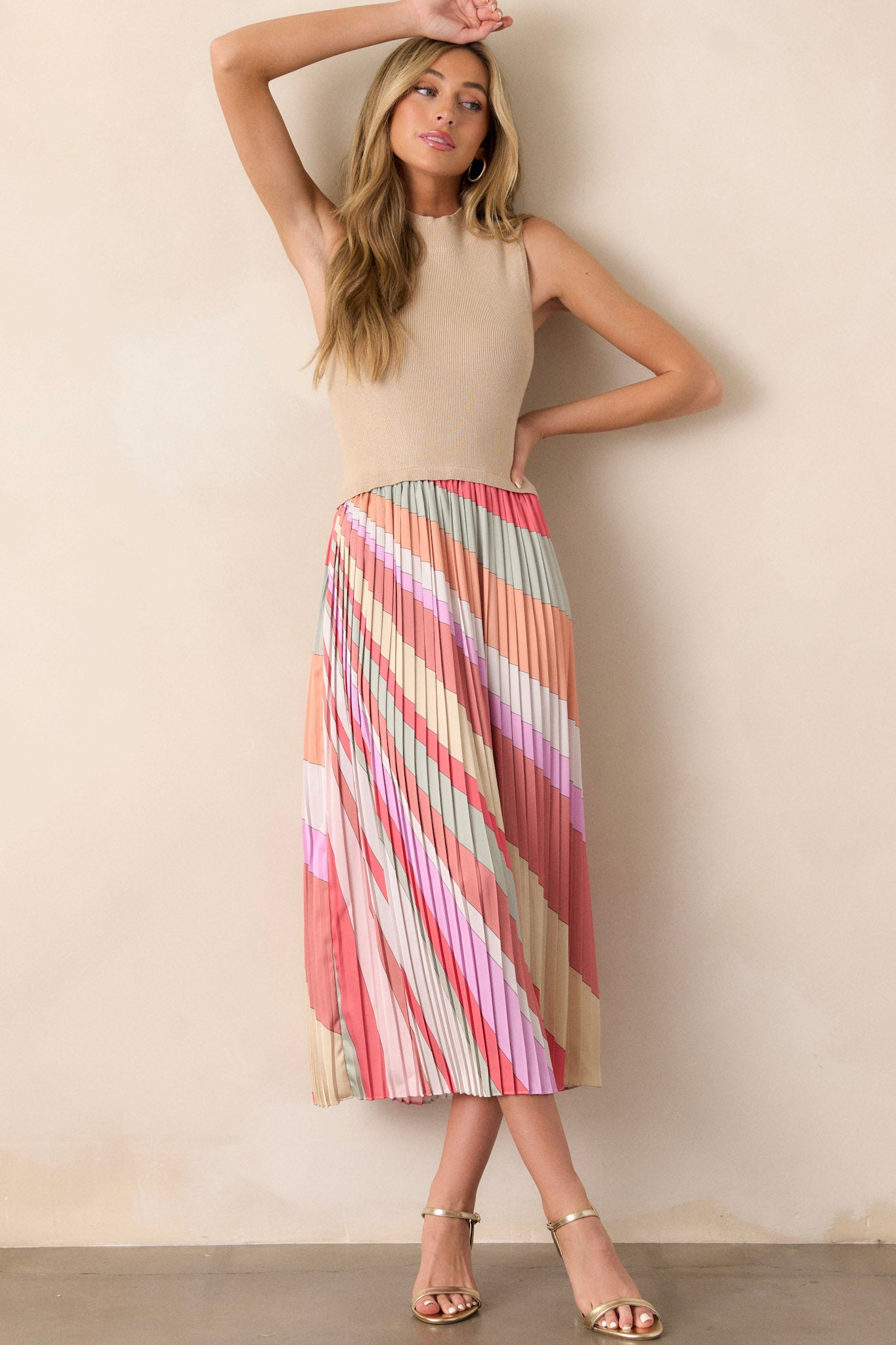 Action shot of a taupe midi dress displaying the fit and movement, highlighting the high neckline, ribbed sweater-like bodice, multi-color pleated skirt, sleeveless design, and flowing silhouette.