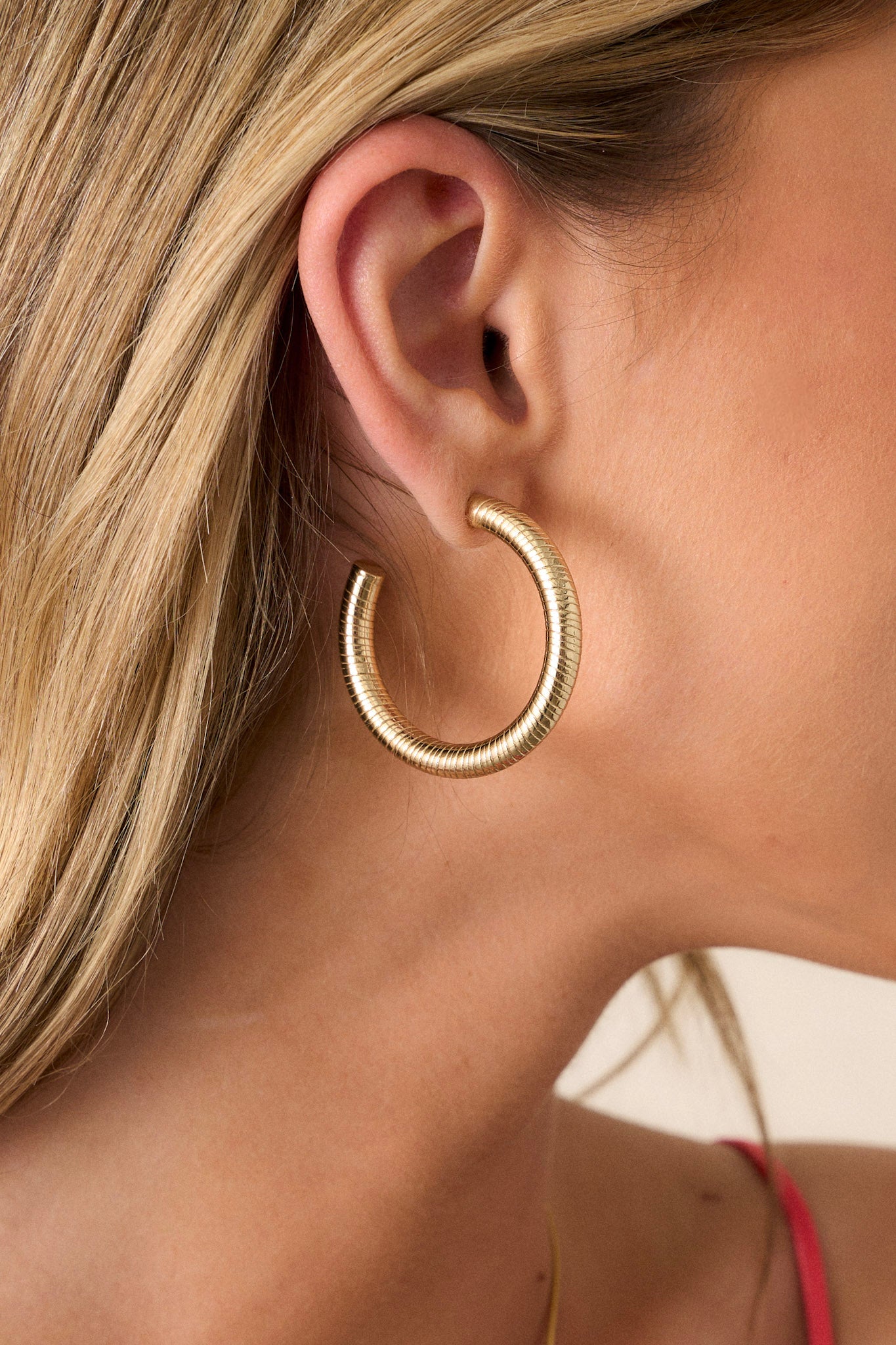 Close-up view of these gold hoop earrings featuring a textured gold finish, and a secure post-back fastening.