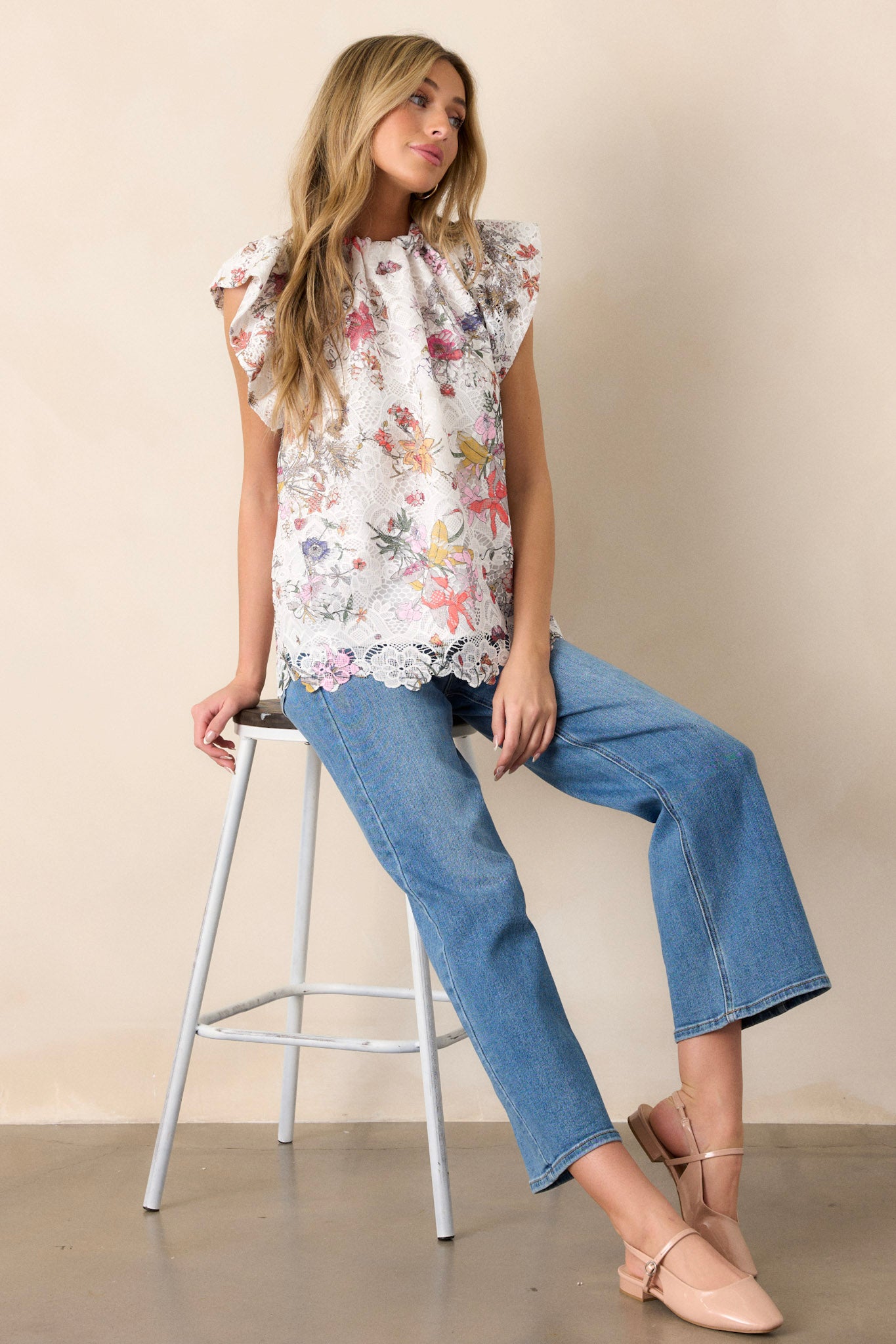 Full length view of a white top with a high neckline, self-tie feature at the back of the neck, floral lace overlay, and ruffled short sleeves.