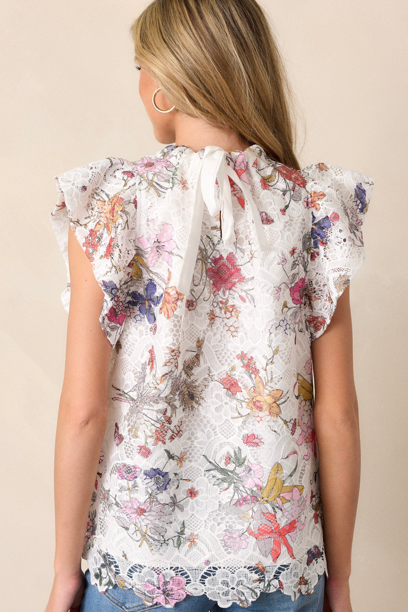 Back view of a white top highlighting the self-tie feature at the back of the neck, floral lace overlay, and ruffled short sleeves.