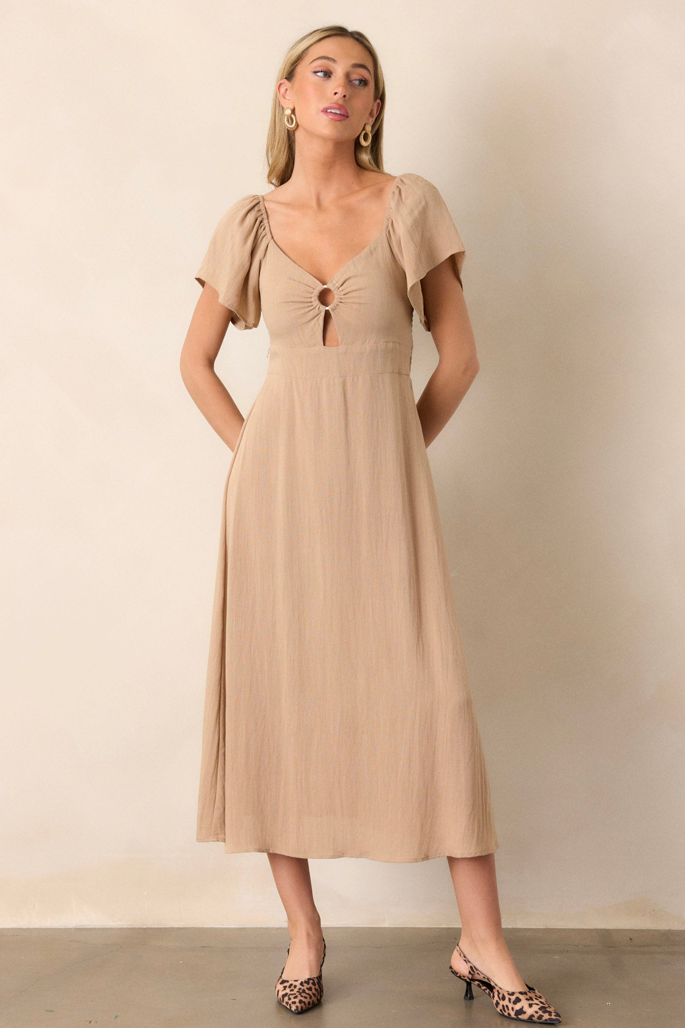 Full length view of a midi dress with a cut-out design in the chest, a smocked back, elastic cuffed puff sleeves, an accent gold ring in the bust, and a flowing silhouette