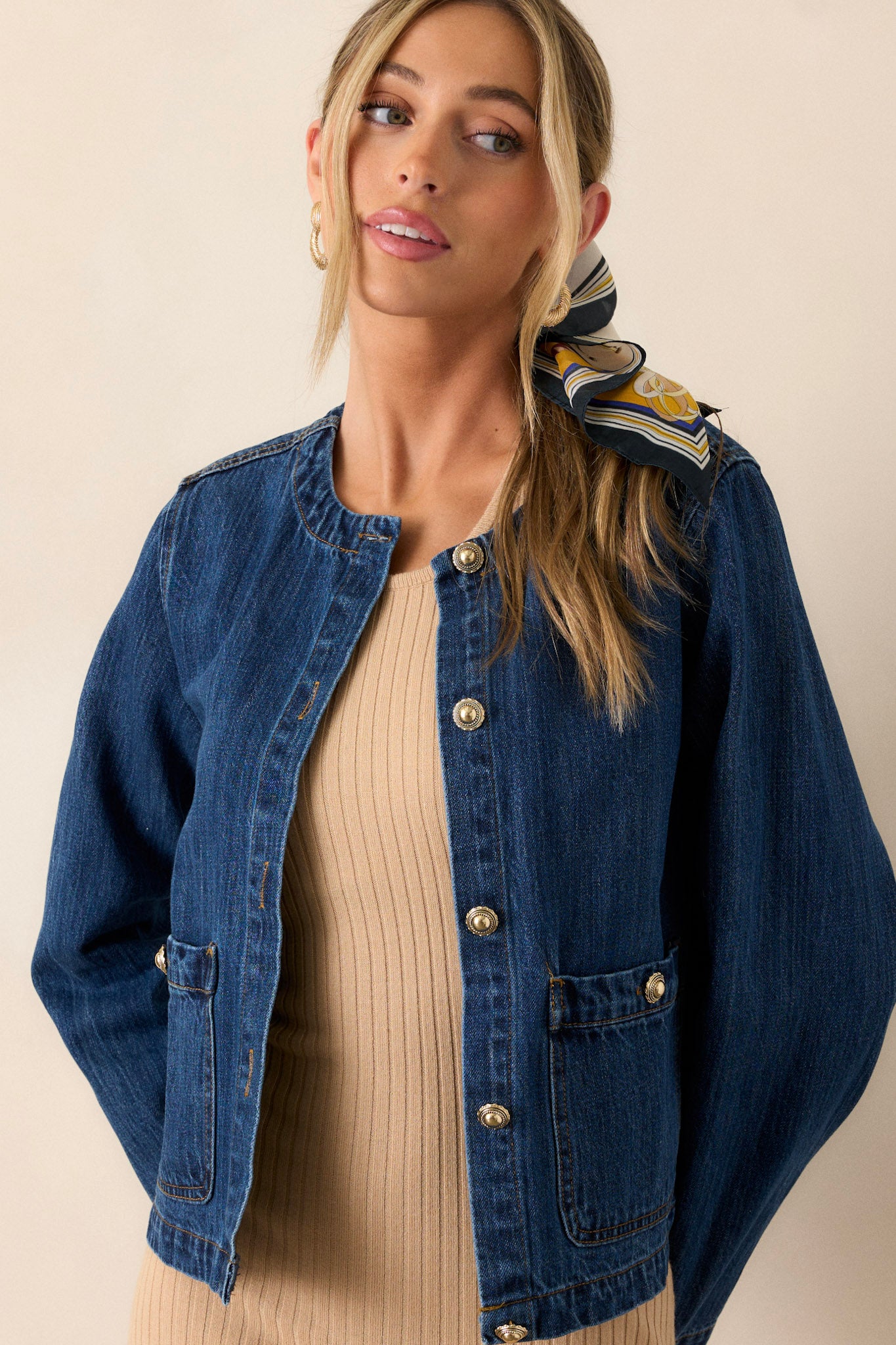 Front view of a dark denim jacket featuring a rounded neckline, a functional button front with gold accent buttons, functional front pockets, and long sleeves.