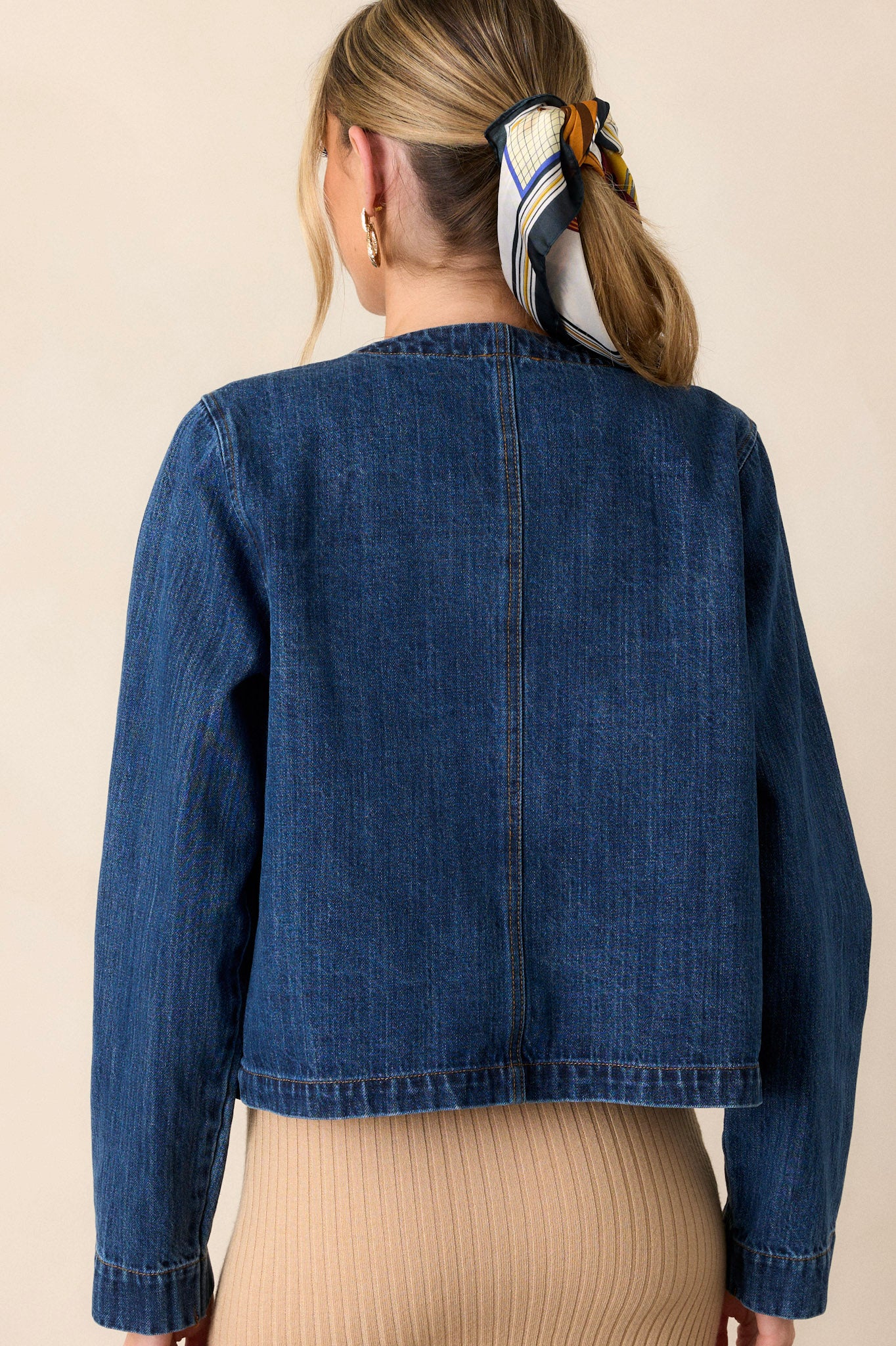 Back view of a dark denim jacket highlighting the rounded neckline, long sleeves, and the back seam detailing.