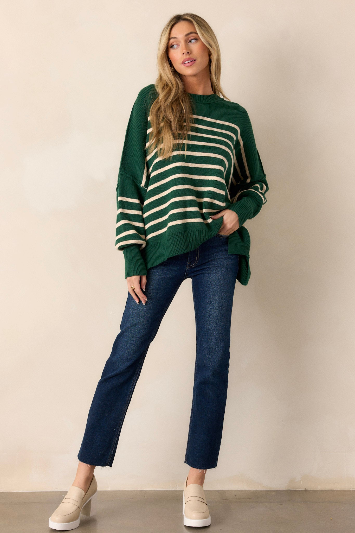 Full length view of a green stripe sweater with a ribbed neckline, an oversized fit, a ribbed hem with side slits, and a horizontal stripe pattern