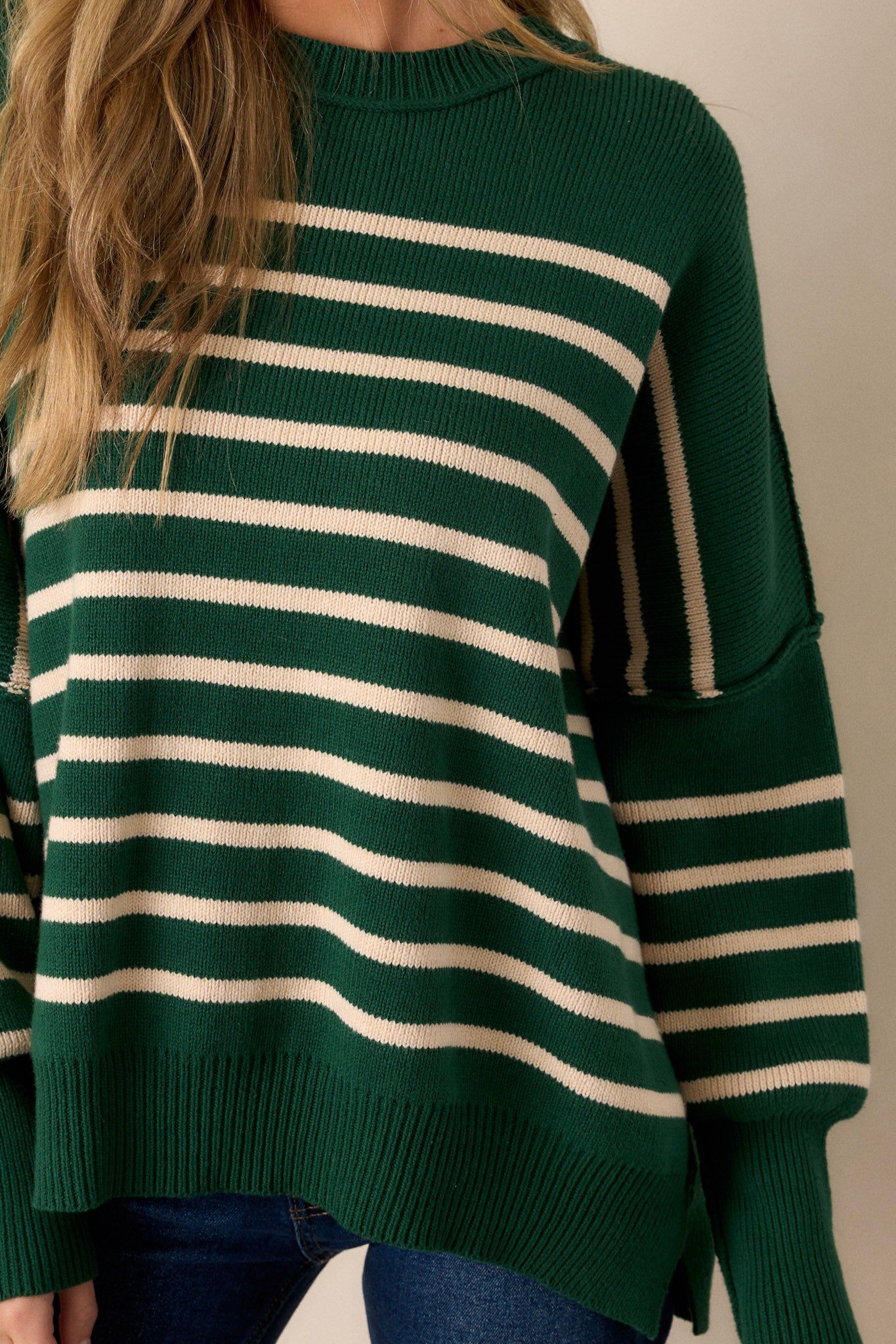 Close-up of the green stripe sweater showing the ribbed neckline, horizontal stripe pattern, and side slits on the ribbed hem.