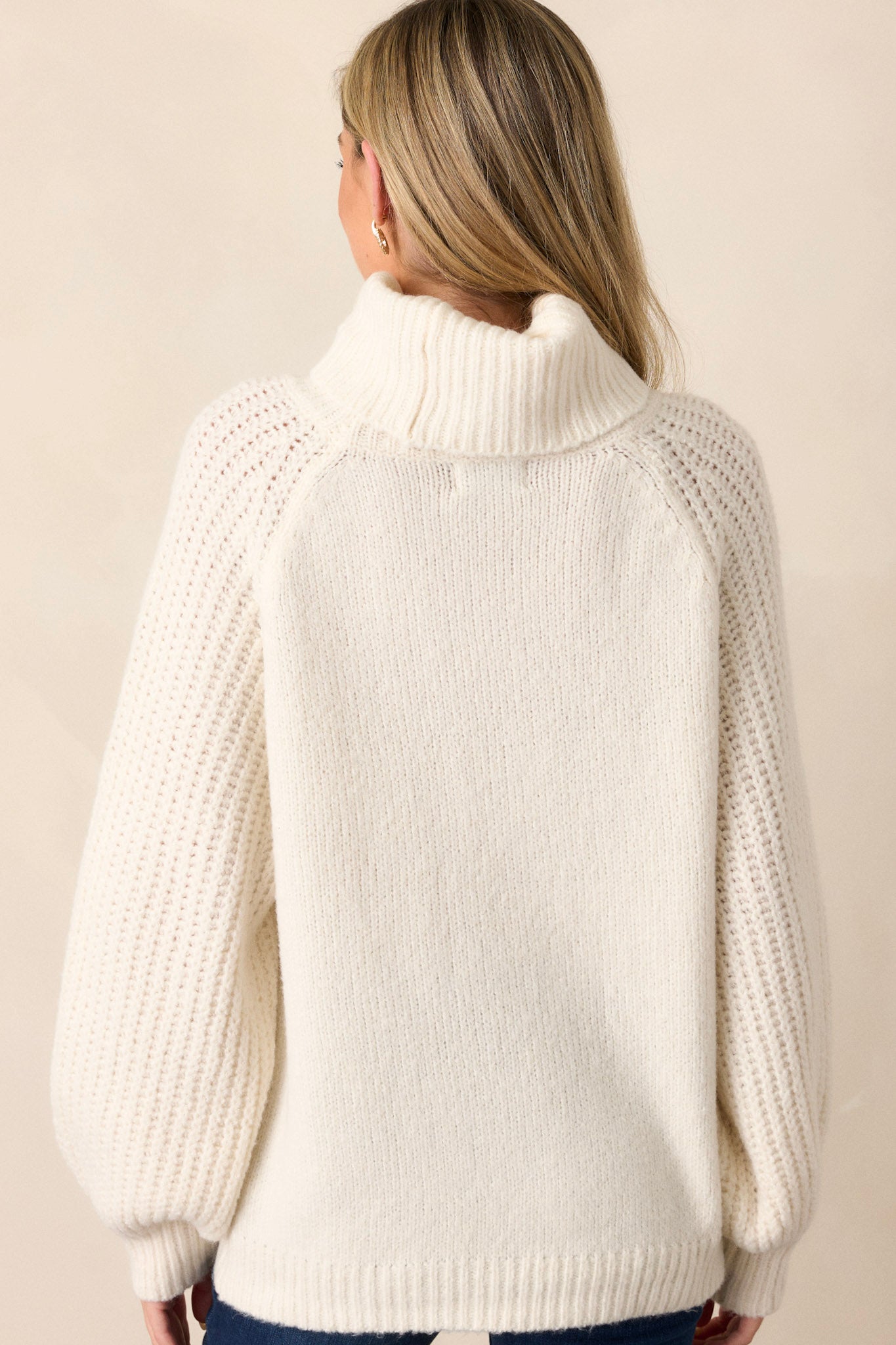 Back view of  this sweater that features a turtleneck, chunky knit bishop sleeves, and a ribbed hemline.