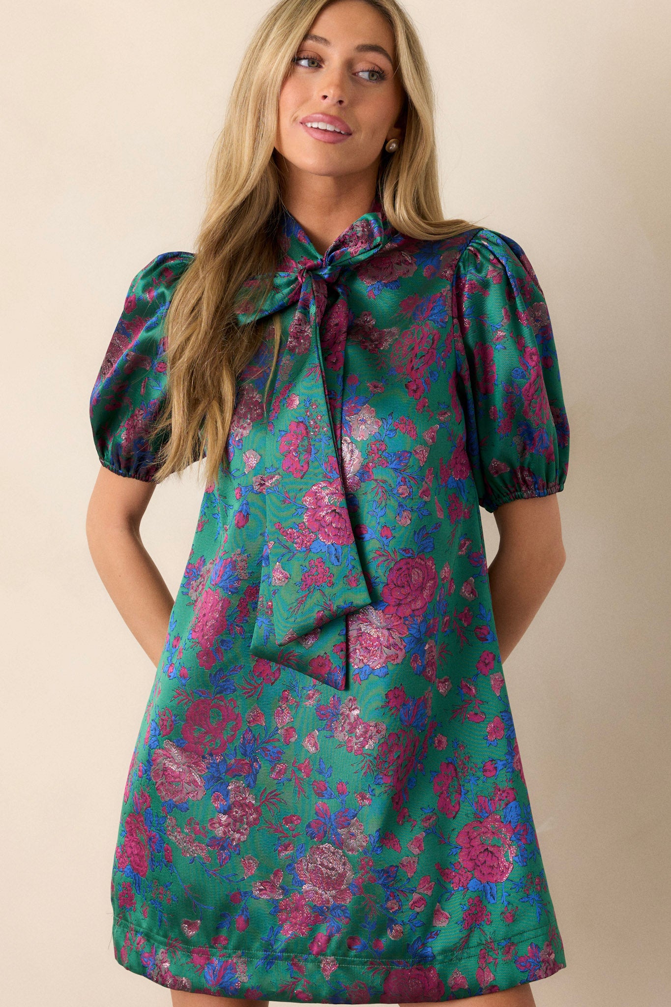 Front view of this green dress that features a tie-neckline, elastic puff sleeves, multi-color jacquard fabric, and a mini length.