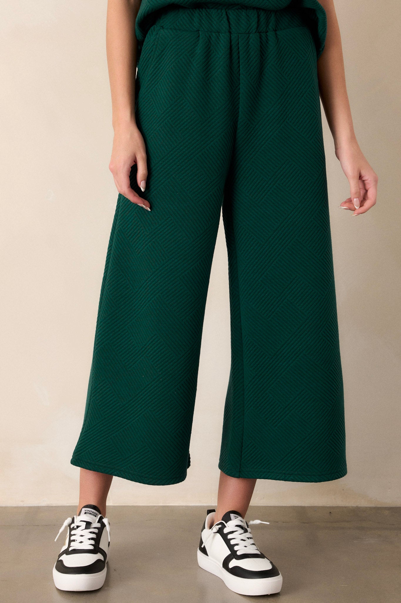 Front view of pants featuring a high waisted design, an elastic waistband, functional hip pockets, a textured crisscross design, and a wide leg