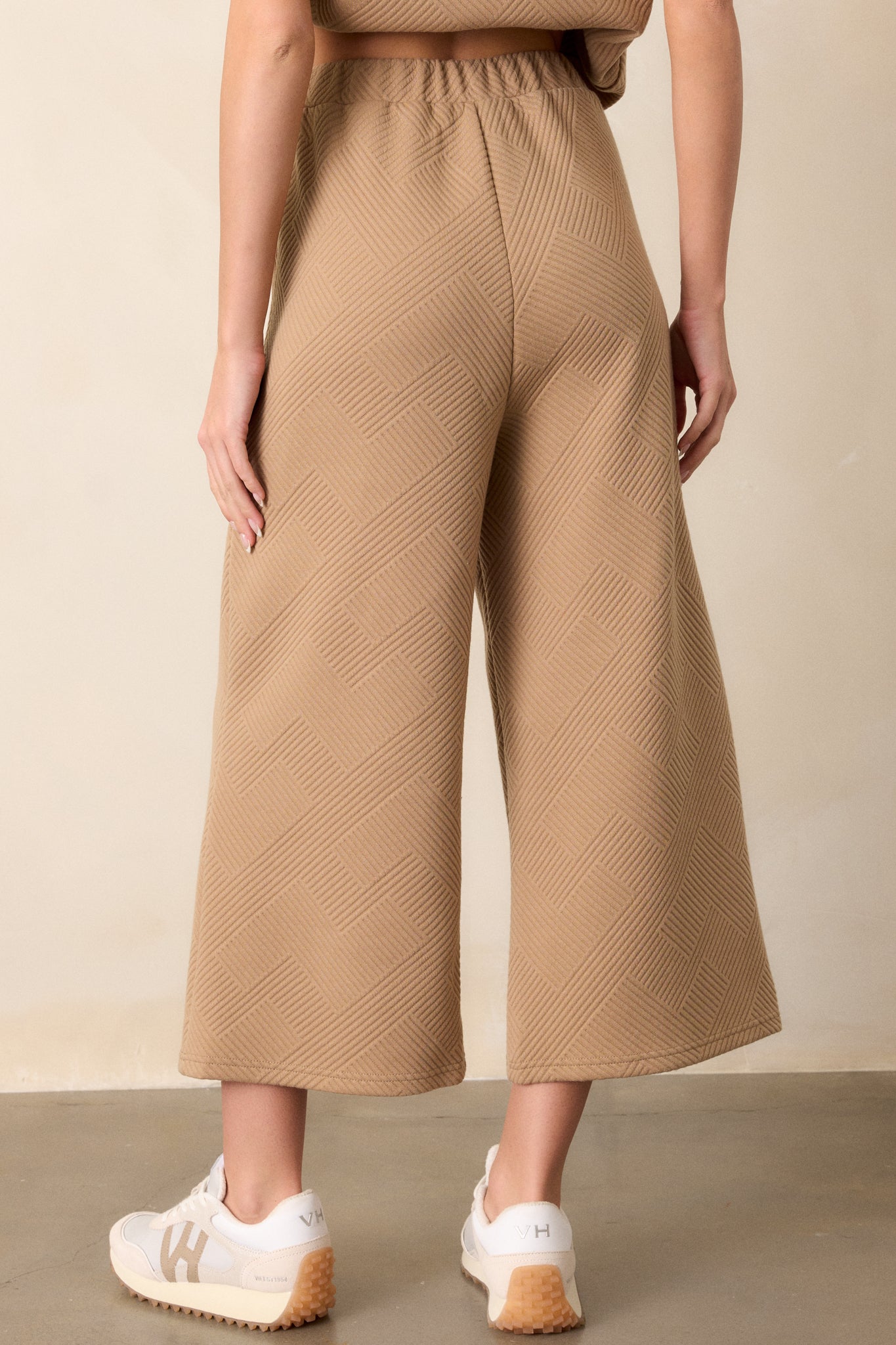 Back view of tan pants with a high-waisted design, elastic waistband, functional hip pockets, and a textured crisscross pattern on a wide-leg cut.