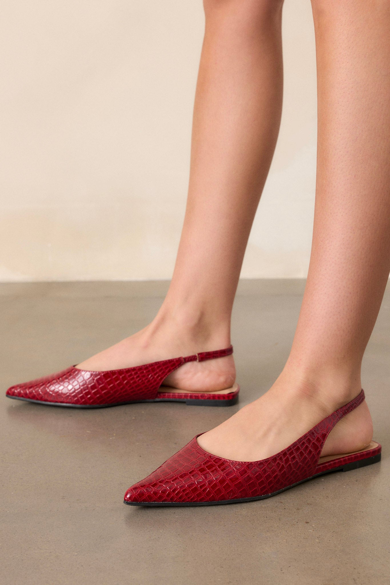 Side view of these red flats featuring a pointed toe, a faux crocodile leather, a slingback-style strap, and a sleek red color.