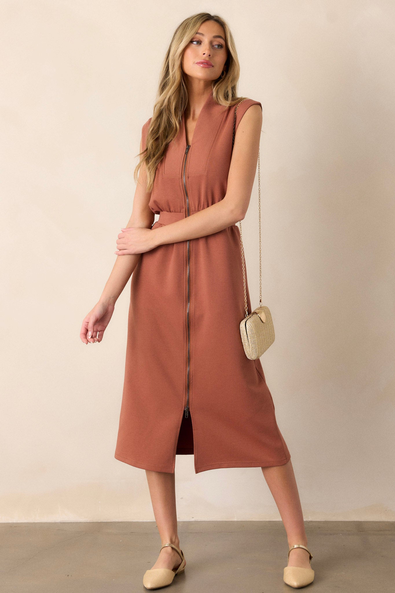 Angled full body of this terracotta dress that features a v-neckline, a slight collar, a functional full zip front, functional hip pockets, and a sleeveless design.