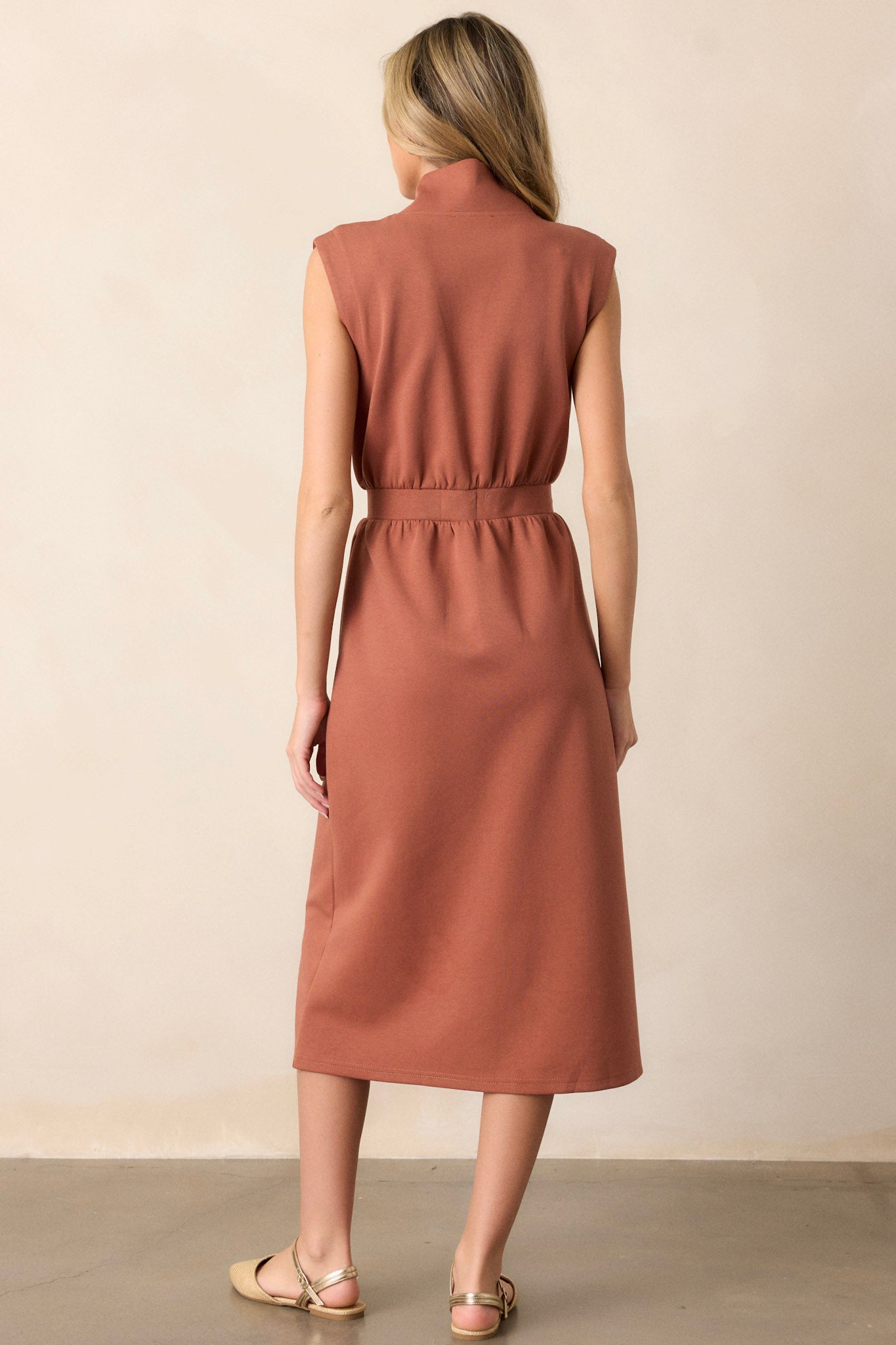 Back view of this terracotta dress that features a v-neckline, a slight collar, a functional full zip front, functional hip pockets, and a sleeveless design.