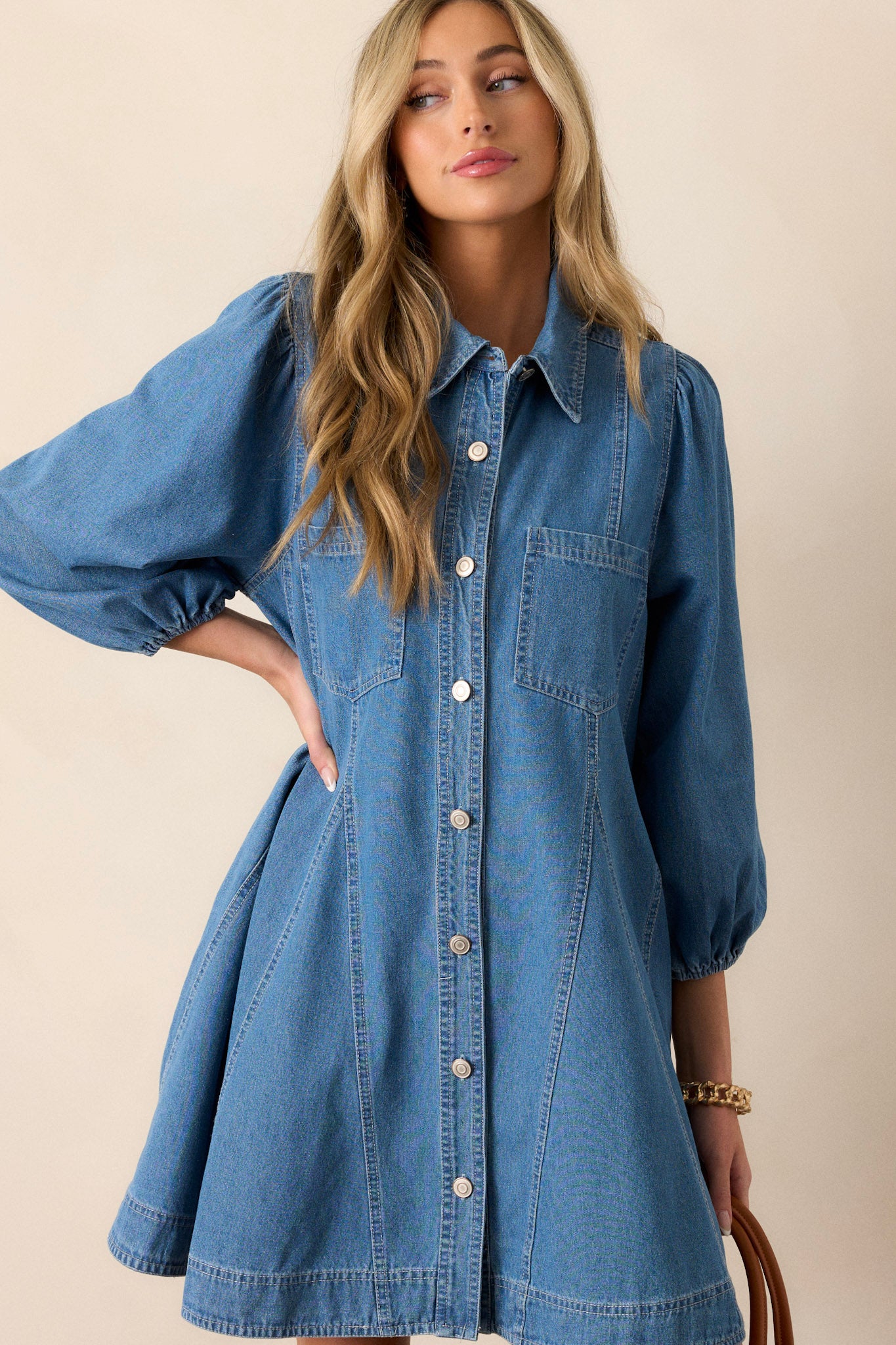 Front angled view of this medium wash denim dress that features a collared neckline, a functional button front, functional chest pockets, functional hip pockets, a relaxed fit and elastic cuffed three-fourth sleeves.