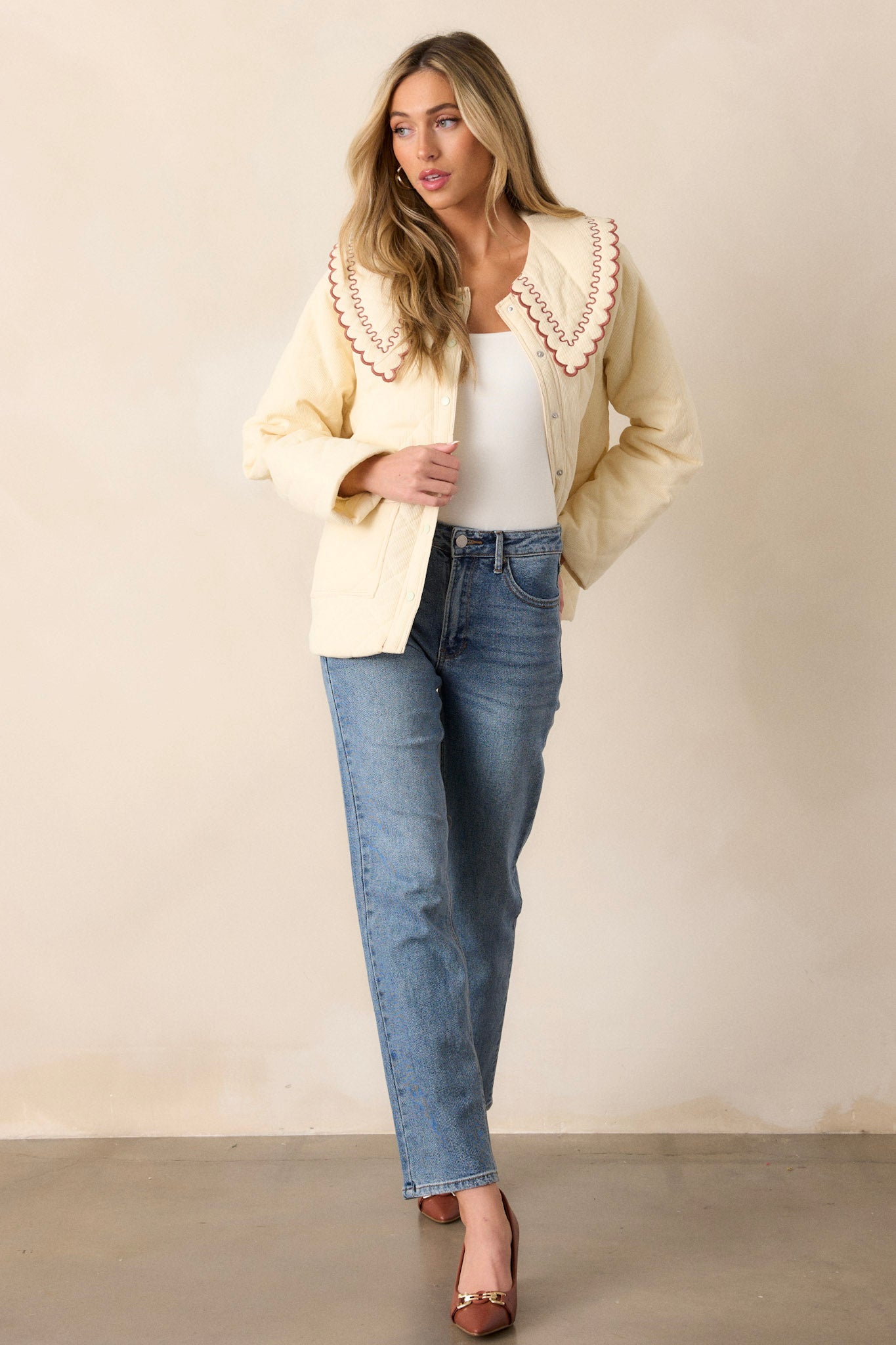 This champagne jacket features a large collared neckline, a burnt orange ruffle trim on the collar, a functional button and snap front, functional hip pockets, and a soft quilted material.