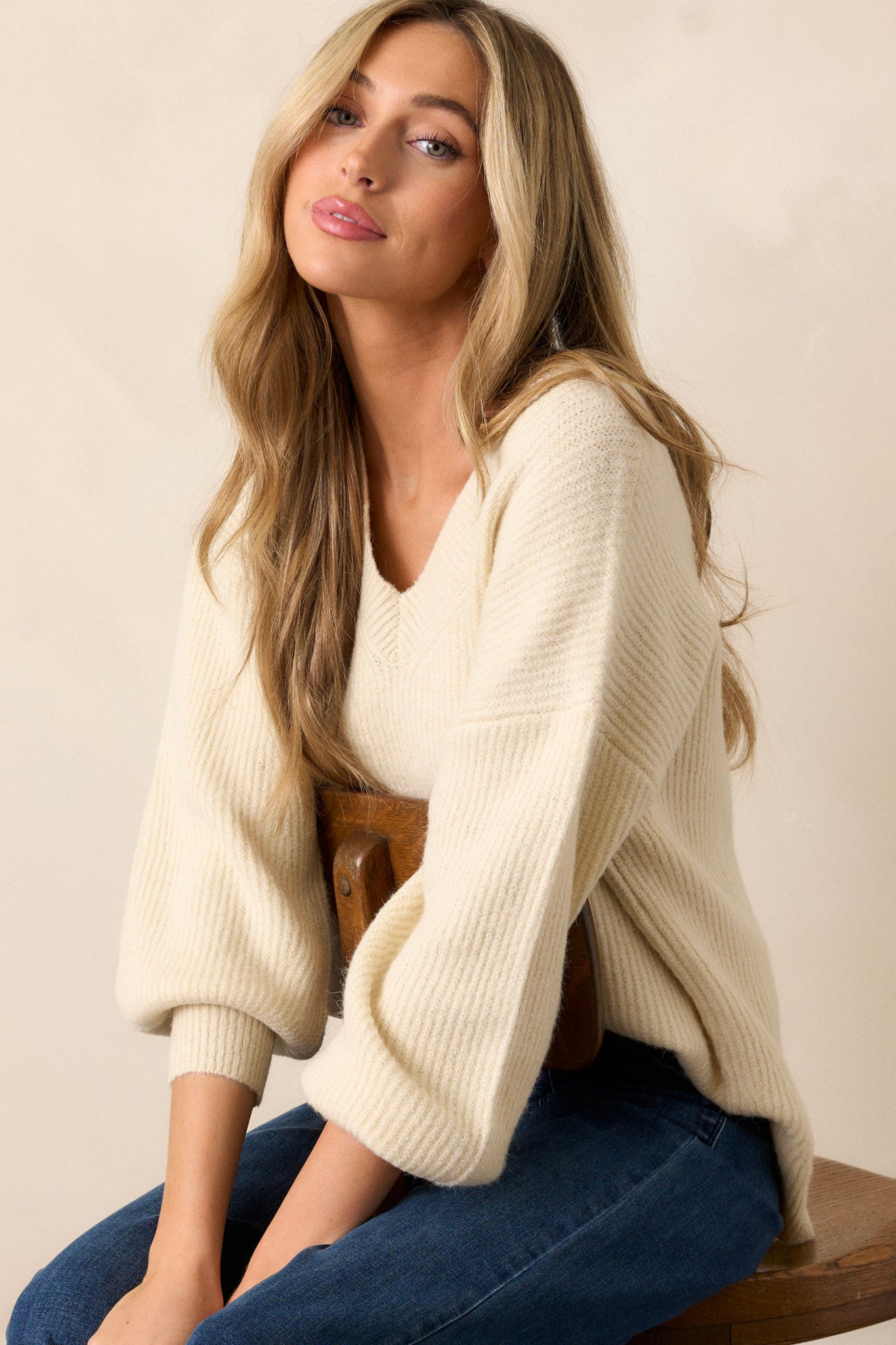 Seated front view of this sweater that features a v-neckline, long sleeves with ribbed cuffs, a ribbed hemline, and slits that go up each side with the back being slightly longer.