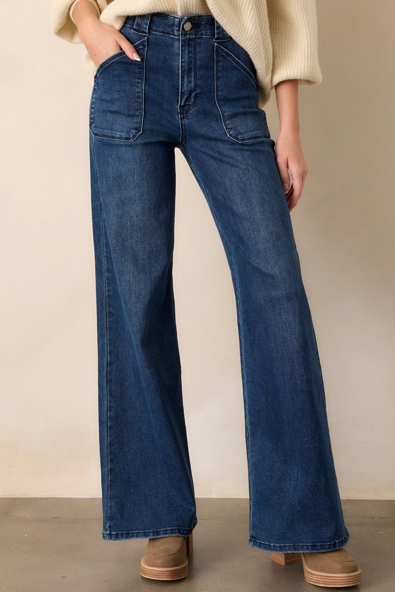 Front view of these dark wash jeans featuring a high waisted design, classic button zipper closure, belt loops, functional front patch pockets, and a flare leg.