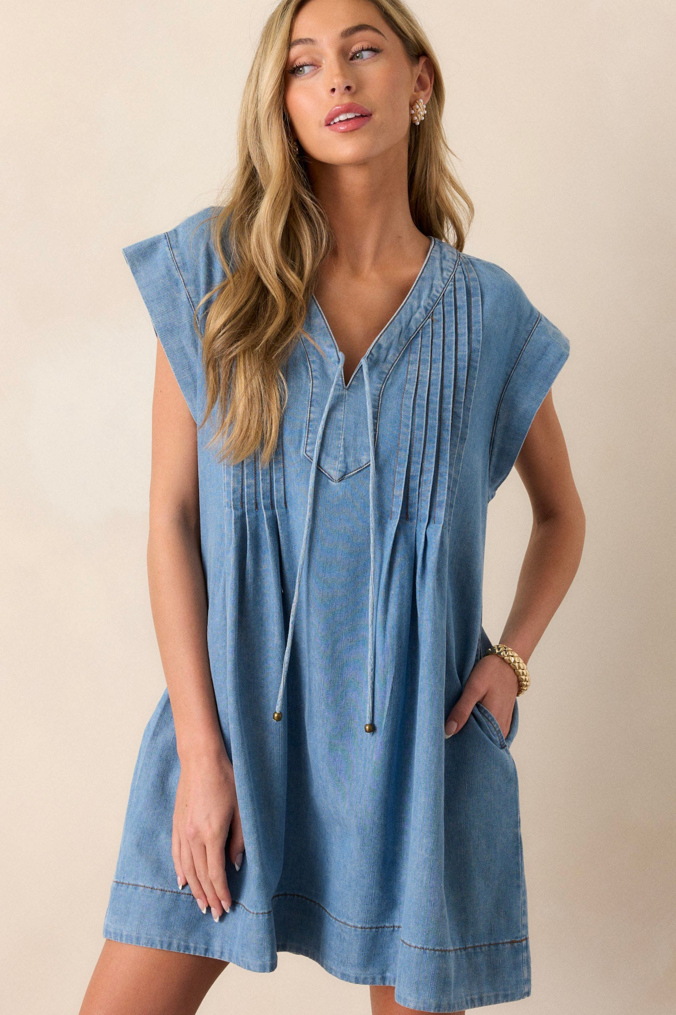 Front view of this chambray dress that features a v-neckline, a self-tie feature, functional pockets, and pin tuck pleating around neckline.