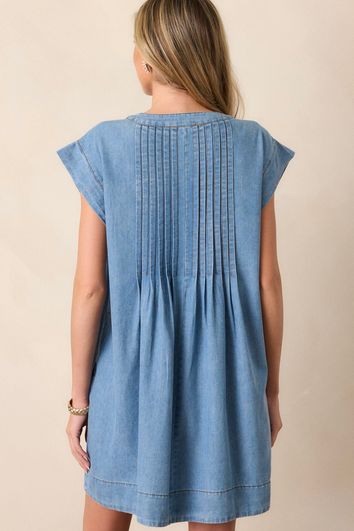 Back of this chambray dress that features a v-neckline, a self-tie feature, functional pockets, and pin tuck pleating around neckline.