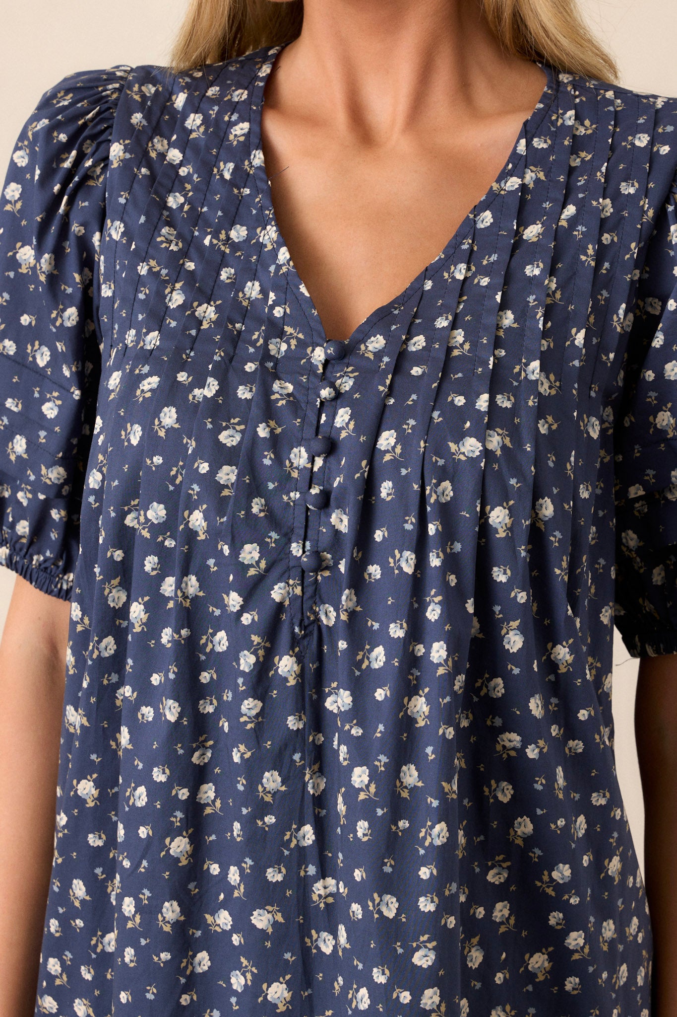 Close-up of this navy dress that  features a v-neckline, pleats in the bust, a relaxed fit, a floral pattern and short puff sleeves.