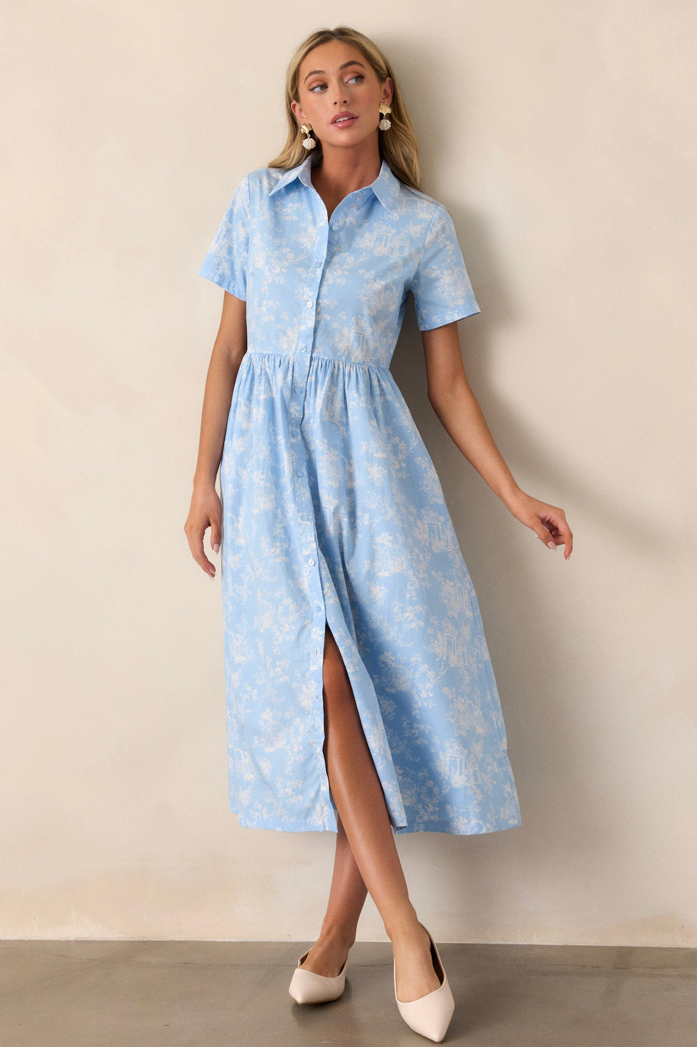 This light blue maxi dress features a collared neckline, a functional button front, gathering at the waist, functional hip pockets, a gorgeous toile pattern, and a flowing silhouette.