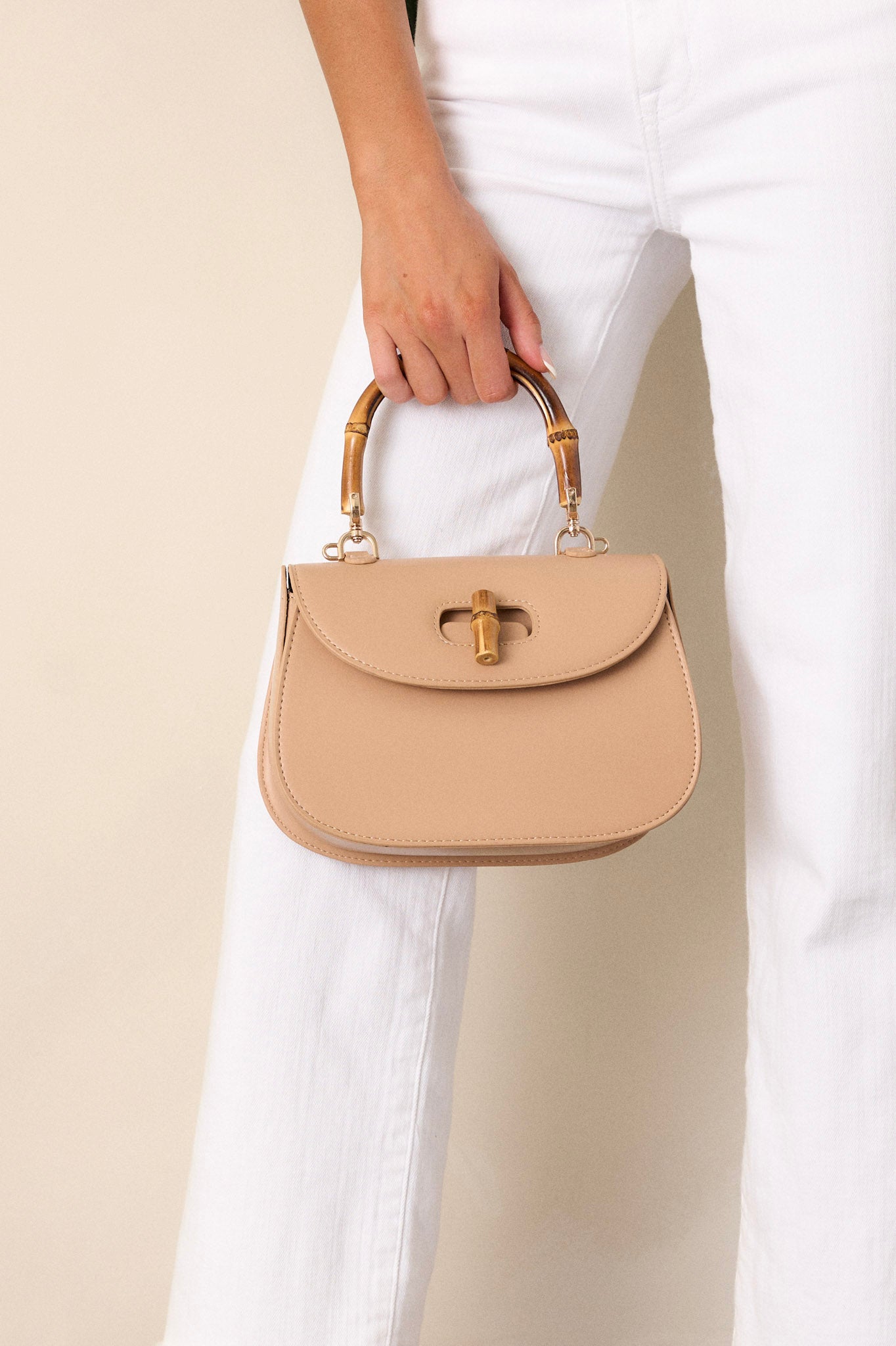 This beige handbag features a single flap design, a bamboo top handle, a bamboo twist lock closure, and a removable strap.