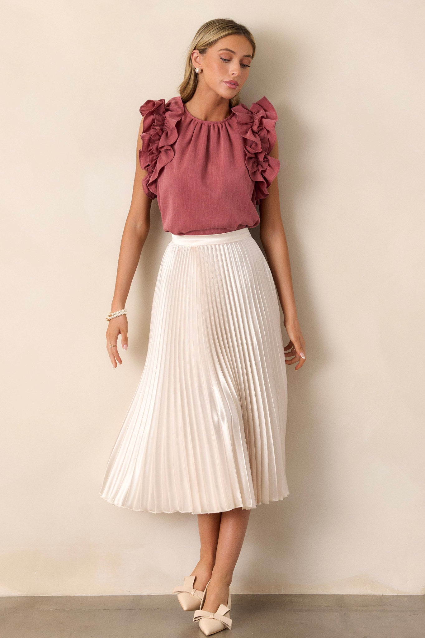 Full length view of an ivory midi skirt featuring a high waisted design, an elastic insert at the back of the waist, a discrete side zipper, and heavy pleating throughout.