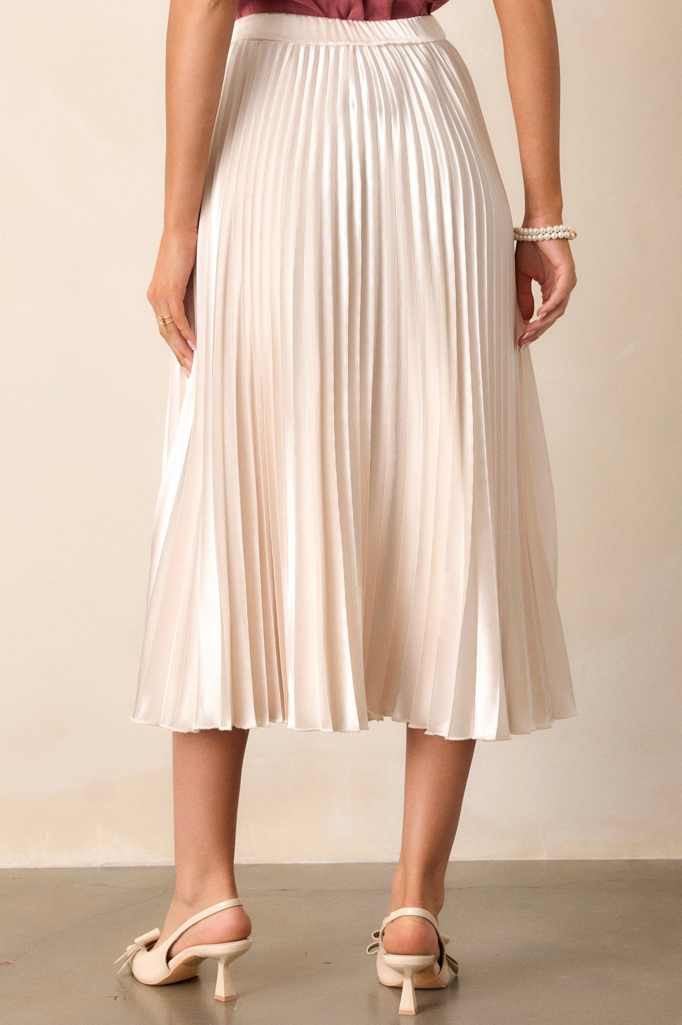 Back view of an ivory midi skirt featuring an elastic insert at the back of the waist, a high waisted design, and heavy pleating throughout.