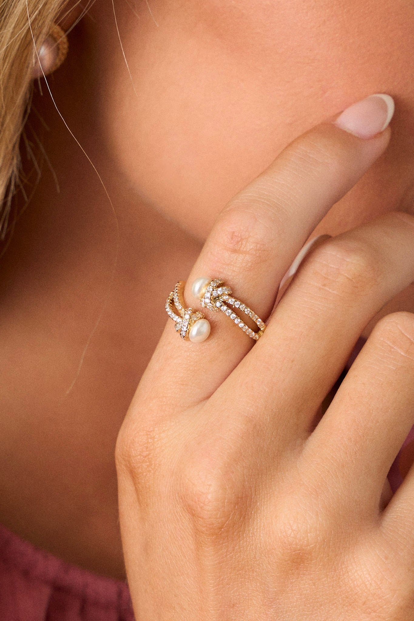 Close-up of this ring that features gold hardware, a twisted design, two pearls, and rhinestones along band.