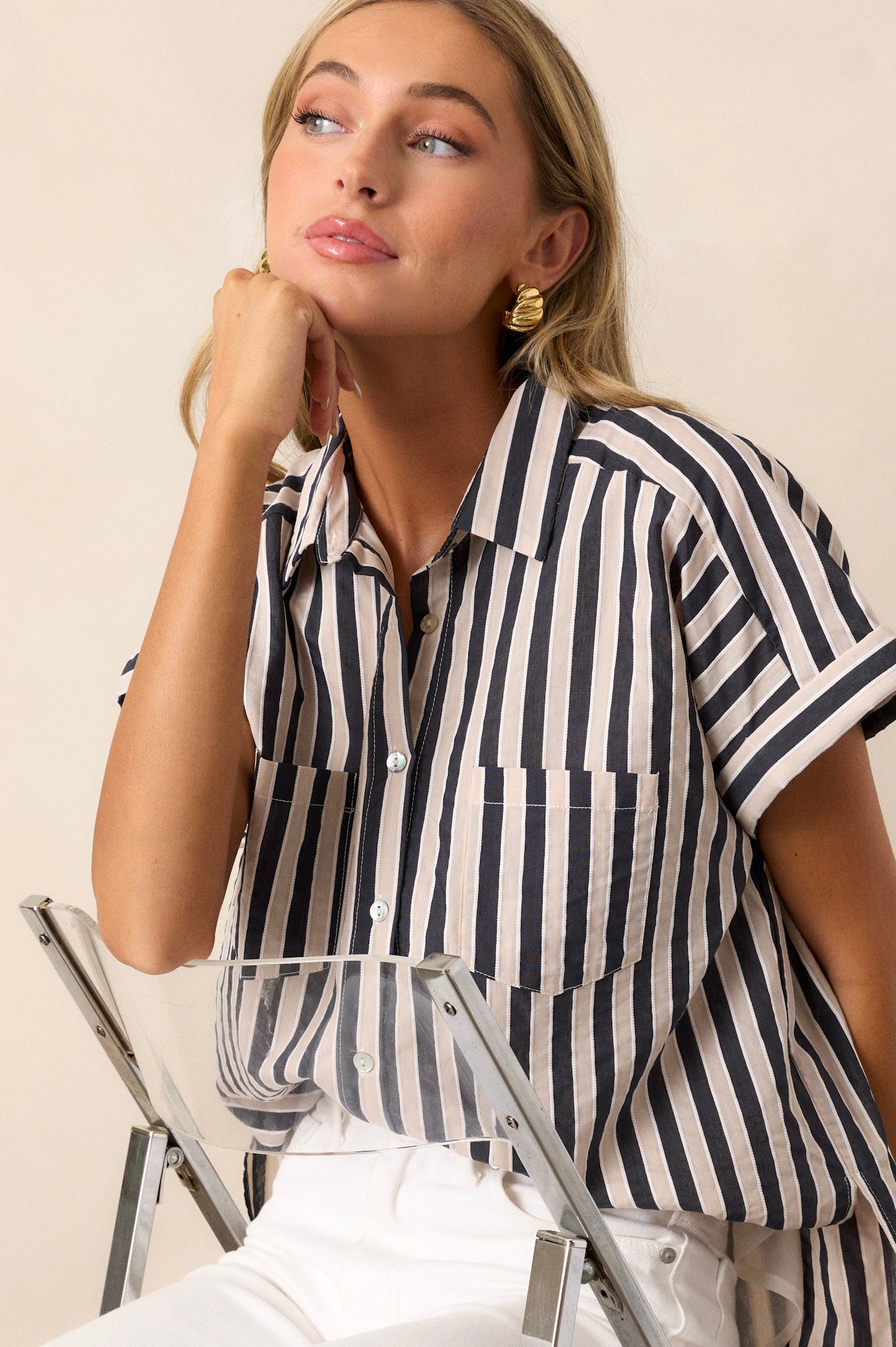 This black stripe top features a collared neckline, a full button front, functional breast pockets, a vertical stripe design, cuffed short sleeves, and a split scooped hemline.