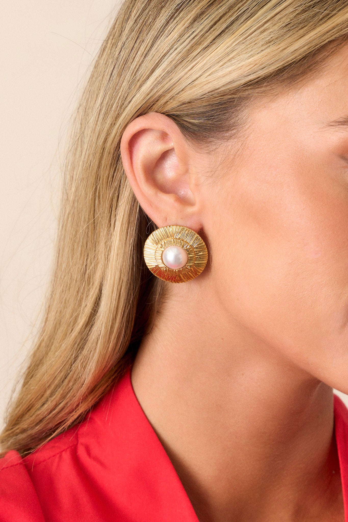 These gold earrings feature a textured circular disc resembling sun rays, an ivory faux pearl center, and a secure post backing.