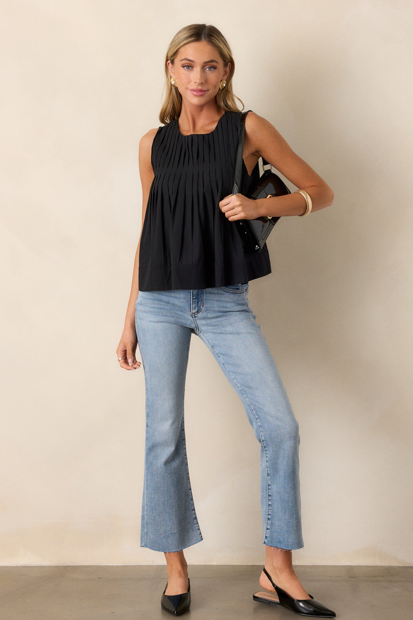 A full-length view showcasing the sleeveless black top, highlighting its round neckline and pleated bust, with the relaxed fit visible.