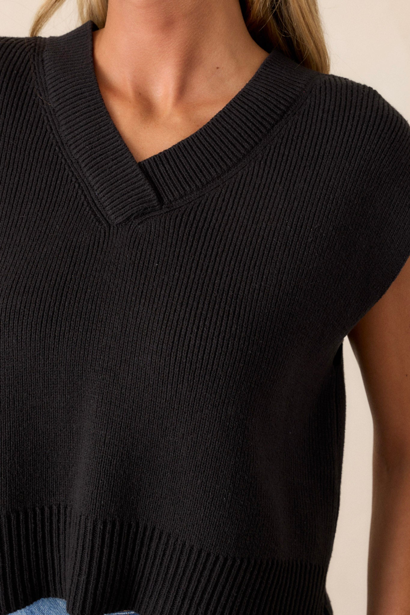 Close-up of the black sweater top showing the v-neckline, knit material, thick hemline, and side slits in the hem.