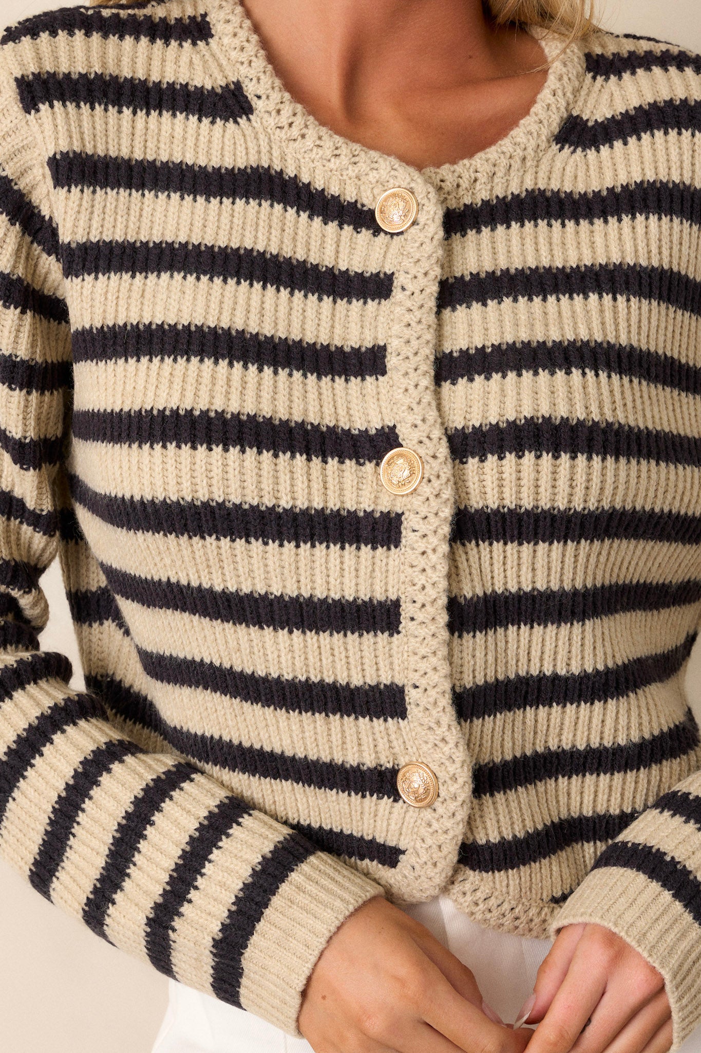 Close-up of the gold-embellished buttons and braided knit detailing along the rounded neckline of the cardigan.