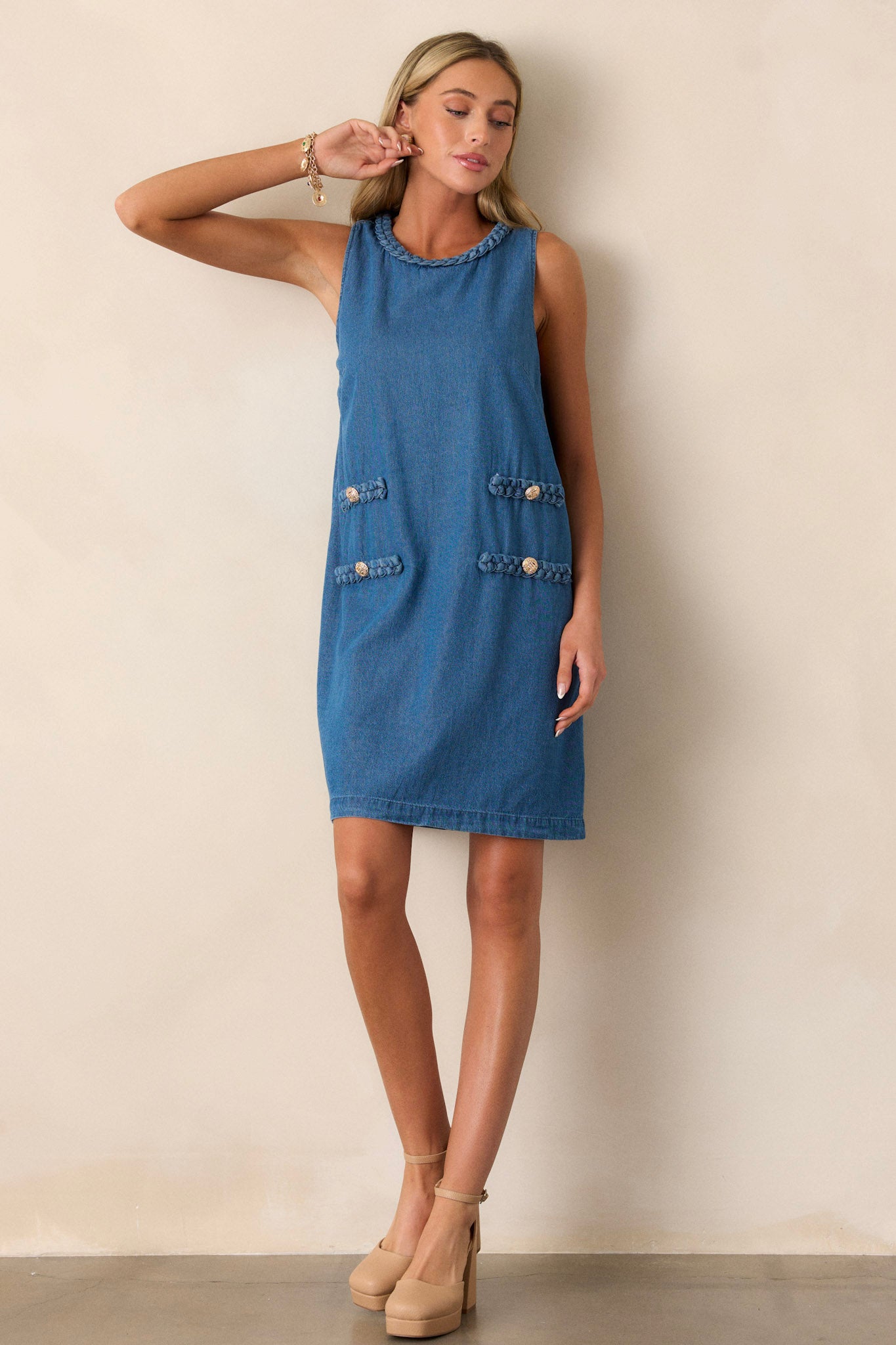 This medium wash dress features a braided crew neckline, a discrete zipper, braided detailing with gold buttons, and a sleeveless design.