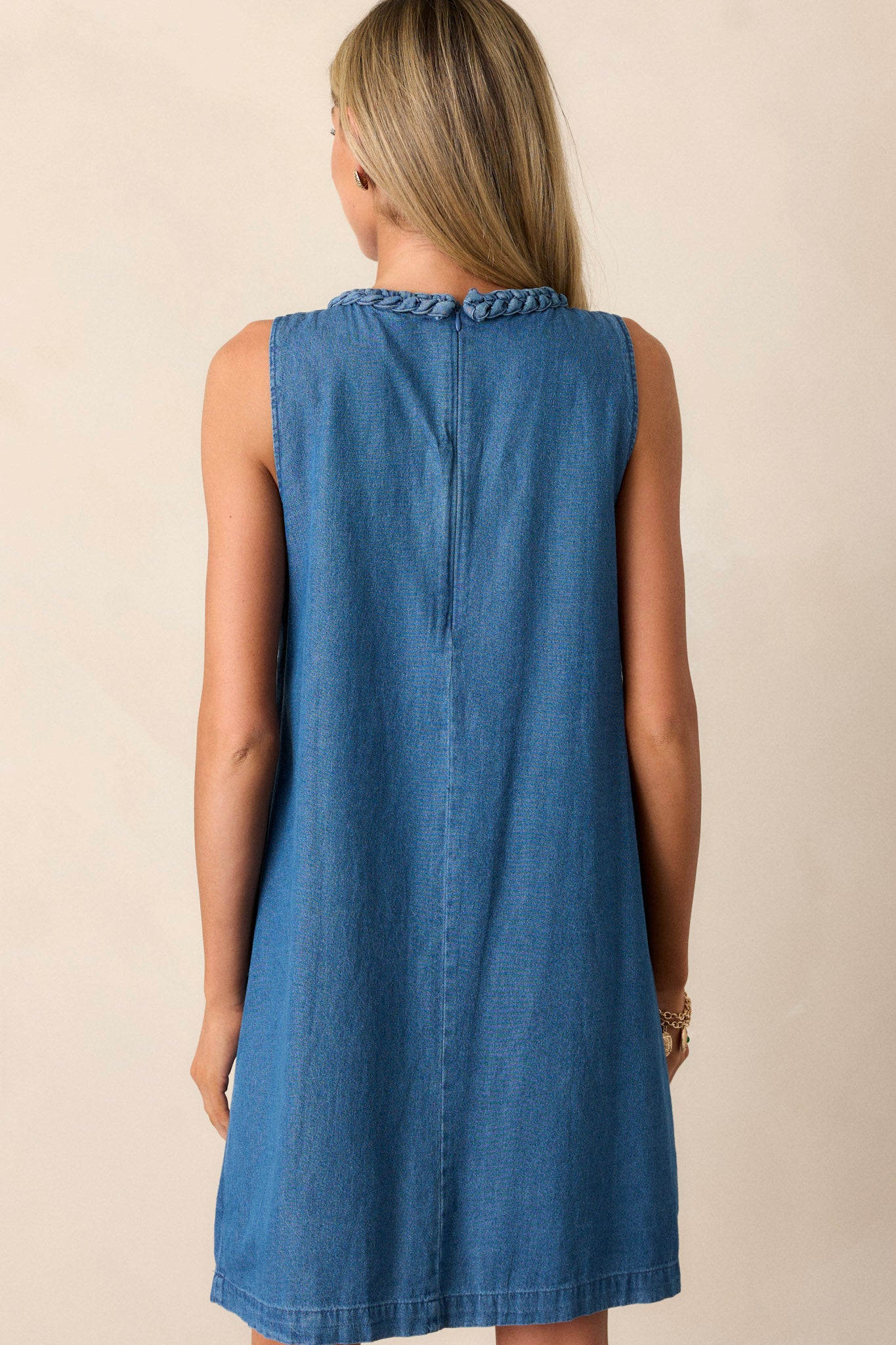 Back view of a medium wash dress highlighting the discrete zipper and sleeveless design.