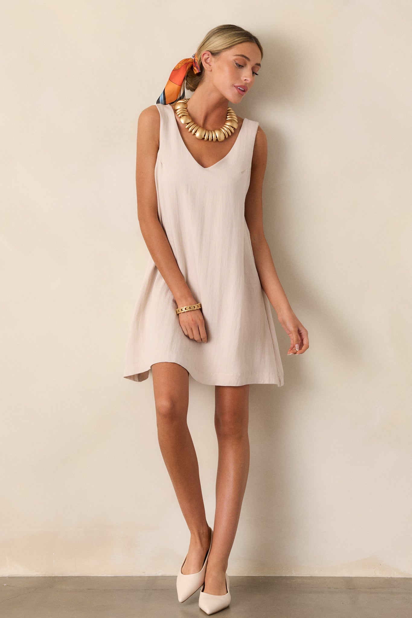 This ivory mini dress features a v-neckline, a sleeveless design, two functional hip pockets, and a shift silhouette.