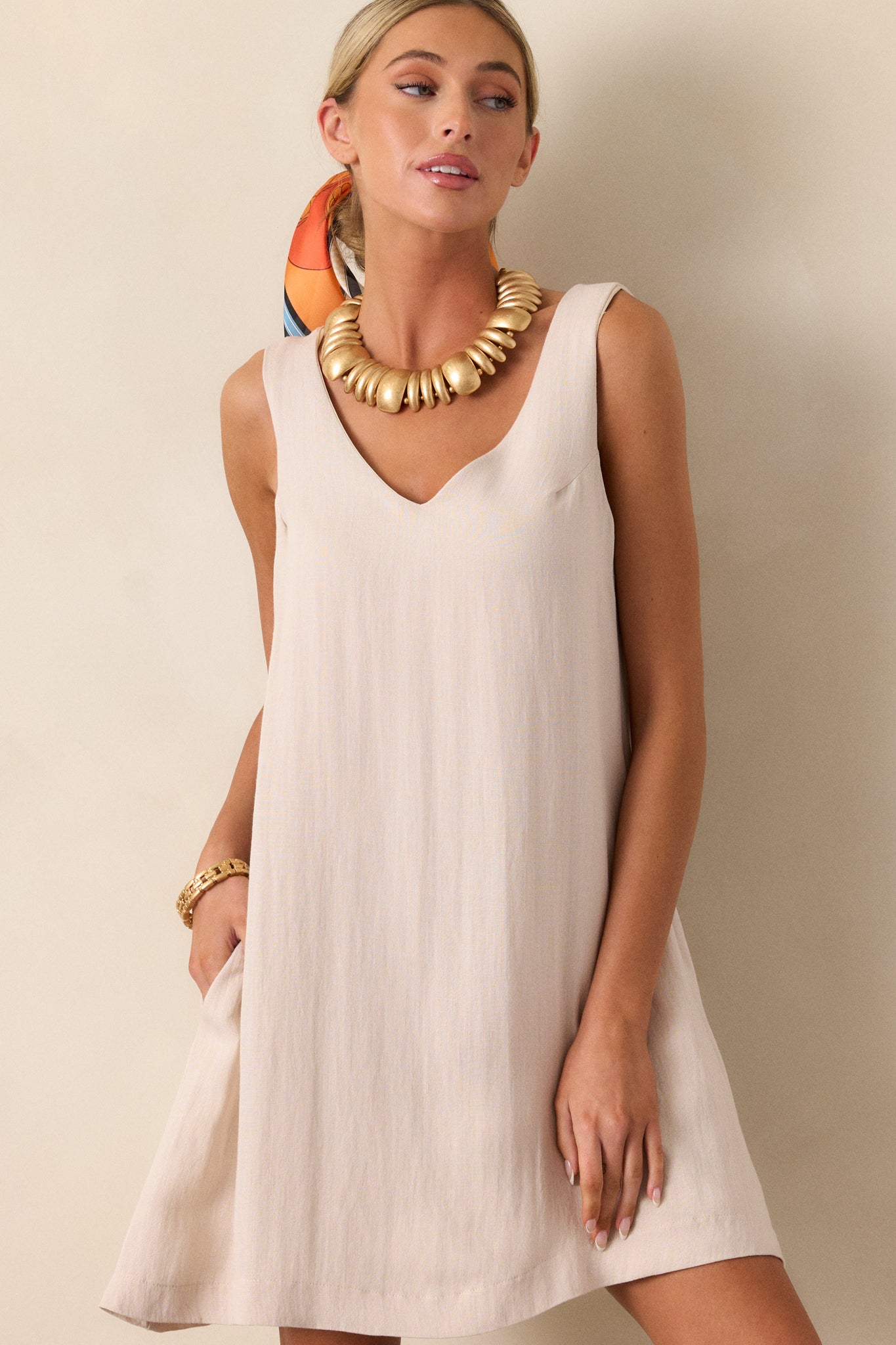 Cropped in view of an ivory mini dress featuring a v-neckline, a sleeveless design, two functional hip pockets, and a shift silhouette.