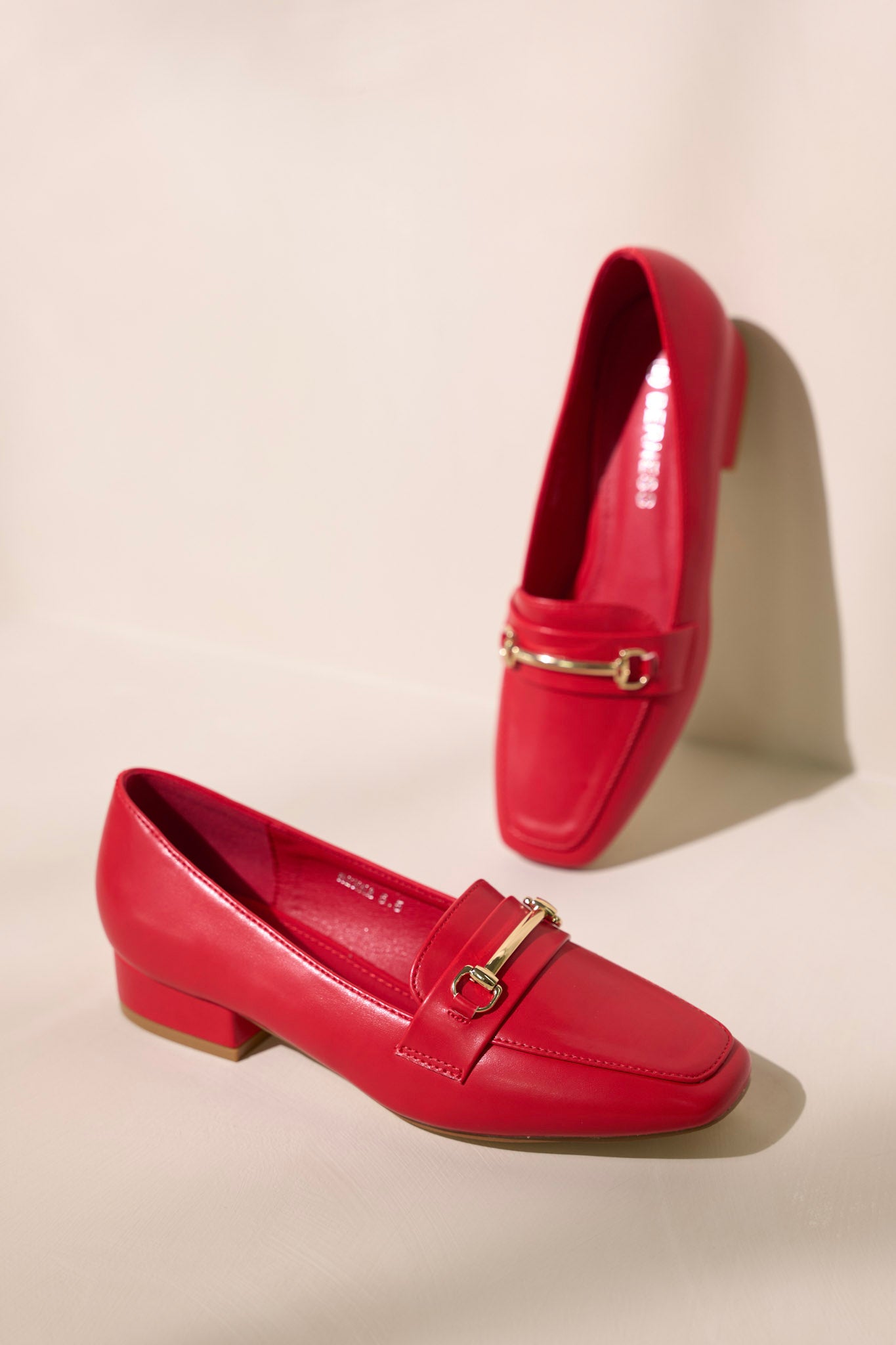 Side view of these red loafers that feature a slip on design, a small heel, a square toe, and gold hardware.