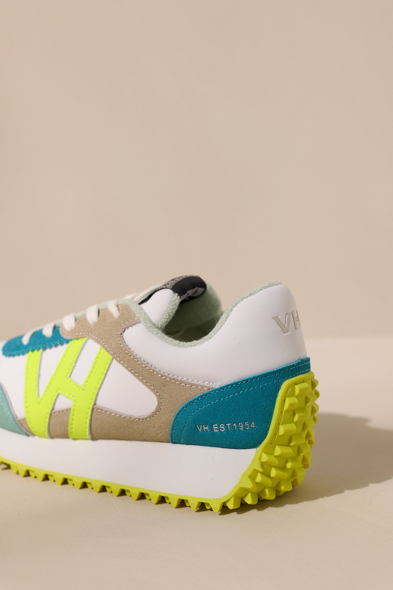 Detailed view of the back of these neon yellow sneakers that feature a rounded toe, functional laces, subtle pops of color, a slight platform, and a heavily textured sole.