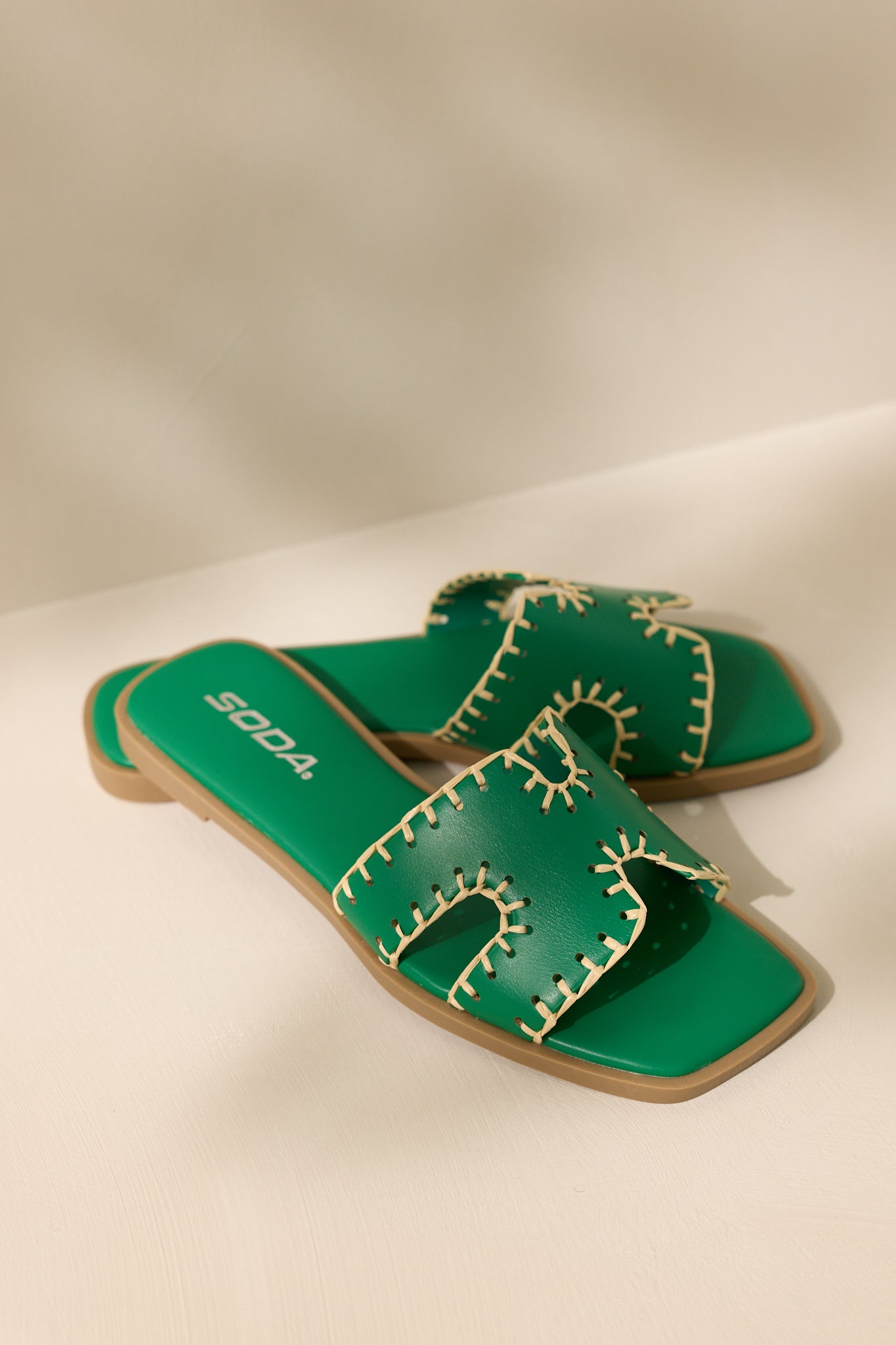 Overhead view of these green sandals that feature a square toe, a slip on design, a strap with cutouts over the top of the foot beige stitch detailing, and a high contrasting sole.