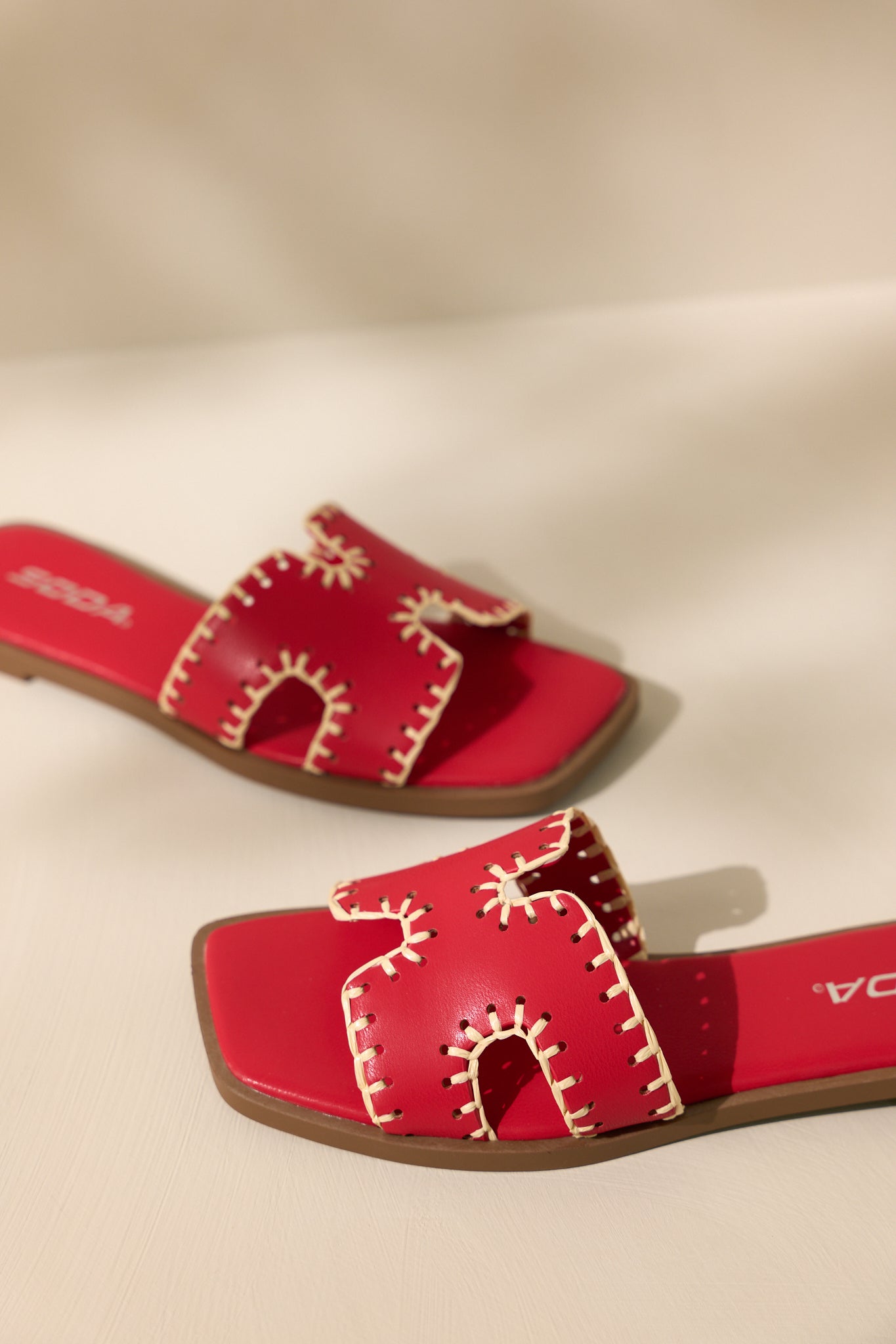 Front view of these red sandals that feature a square toe, a slip on design, a strap with cutouts over the top of the foot beige stitch detailing, and a high contrasting sole.