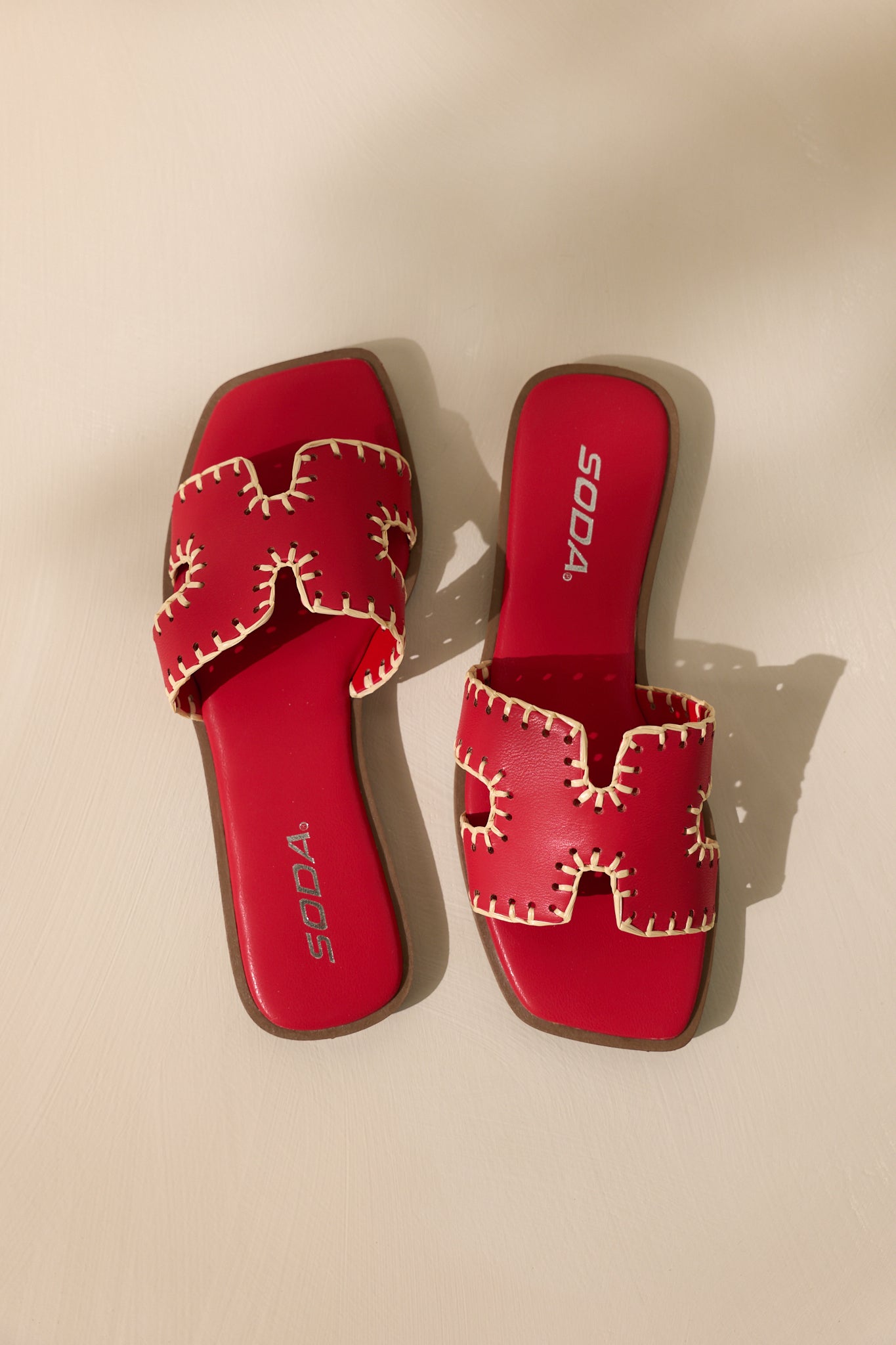 Overhead view of these red sandals that feature a square toe, a slip on design, a strap with cutouts over the top of the foot beige stitch detailing, and a high contrasting sole.