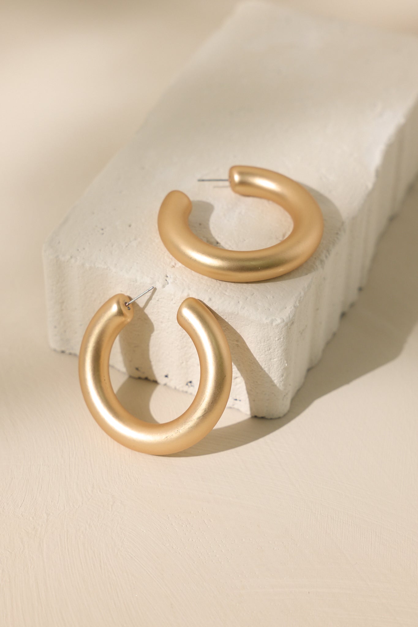 Stand alone view of these gold hoop earrings featuring a matte gold finish, thick design, and a secure post backing.