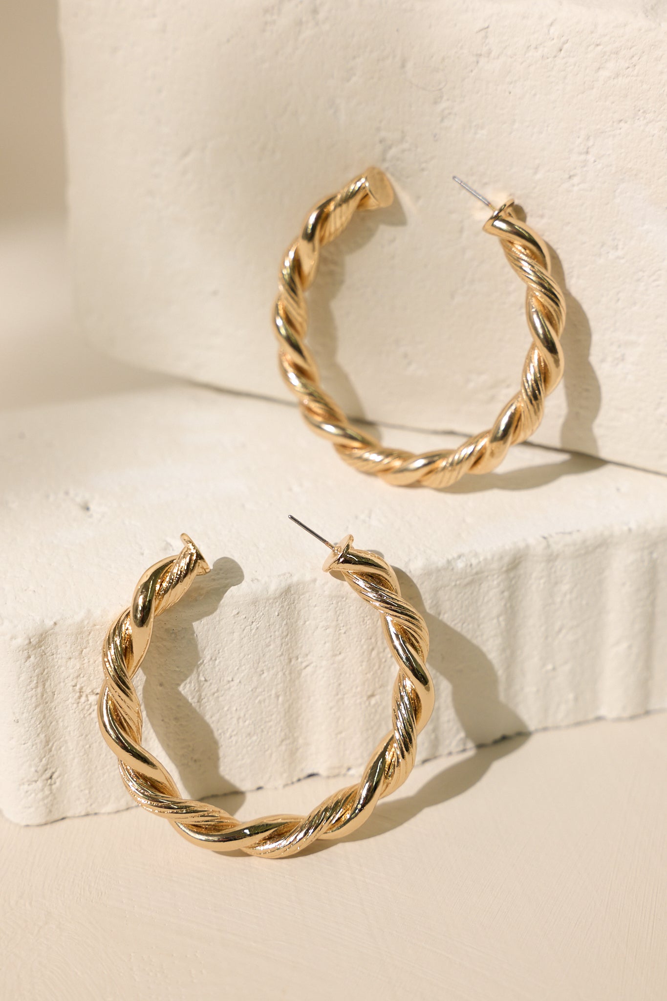 Stand alone view of these gold earrings that feature an incomplete hoop design, a textured twisted design, and secure post backings.