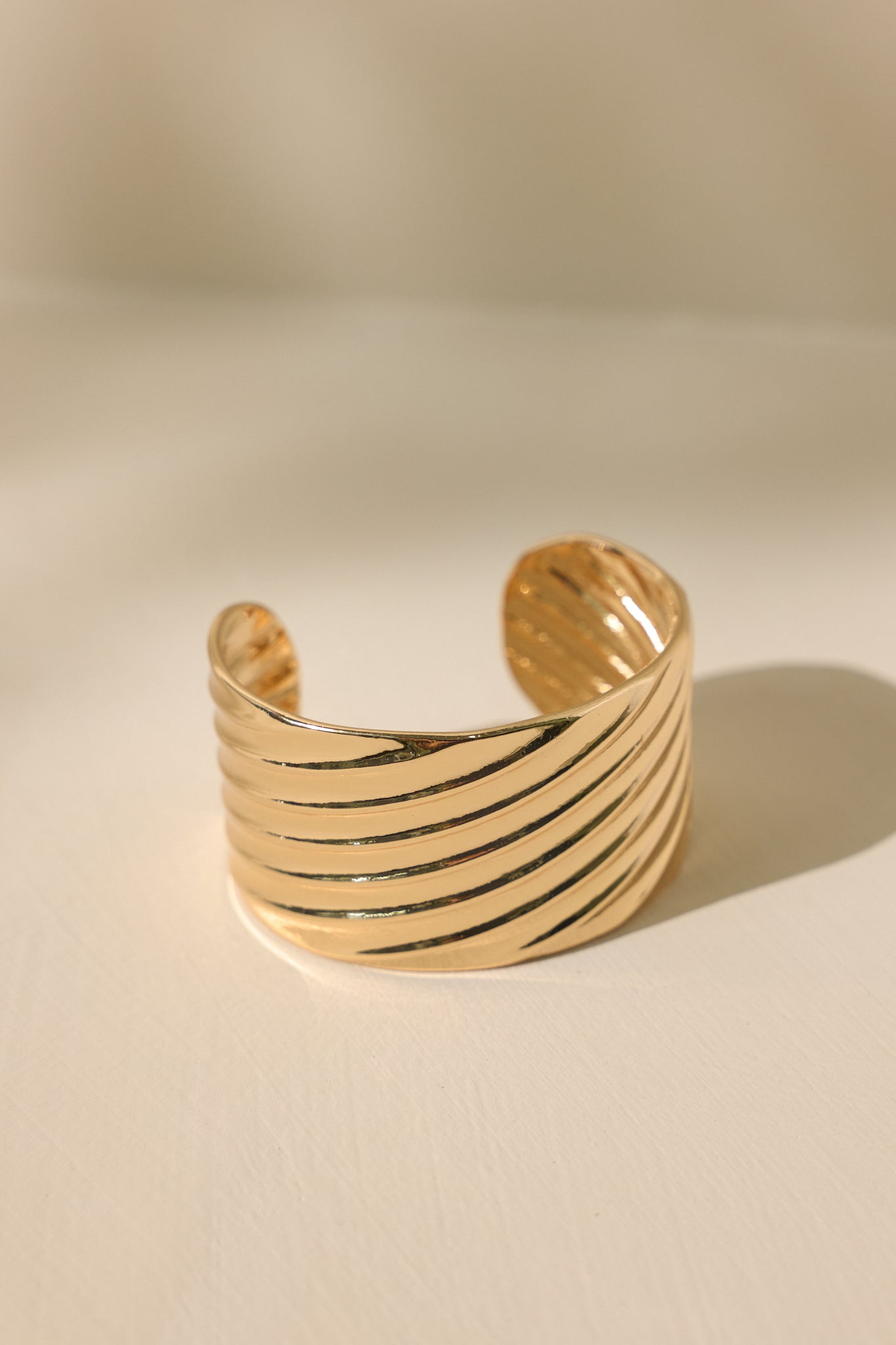 Close-up detailed shot of this gold cuff that features shiny hardware, a textured material, a thick band, and rounded edges.