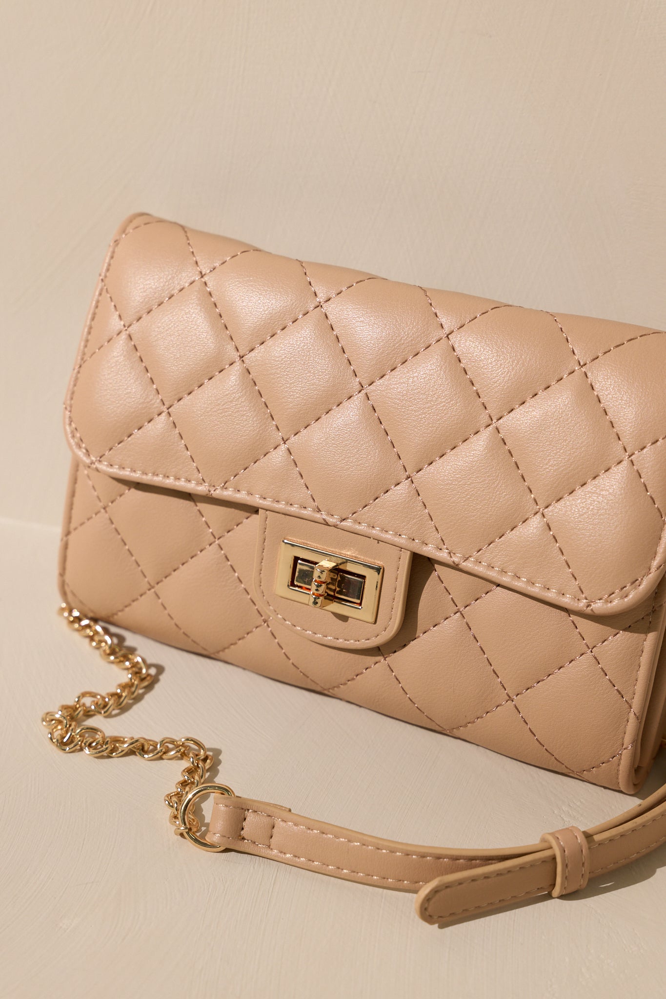 Front view of a beige quilted clutch bag with a front turn-lock closure.